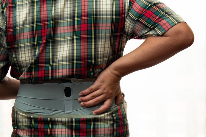 Un uomo con una camicia a quadri si tiene la schiena dolorante.