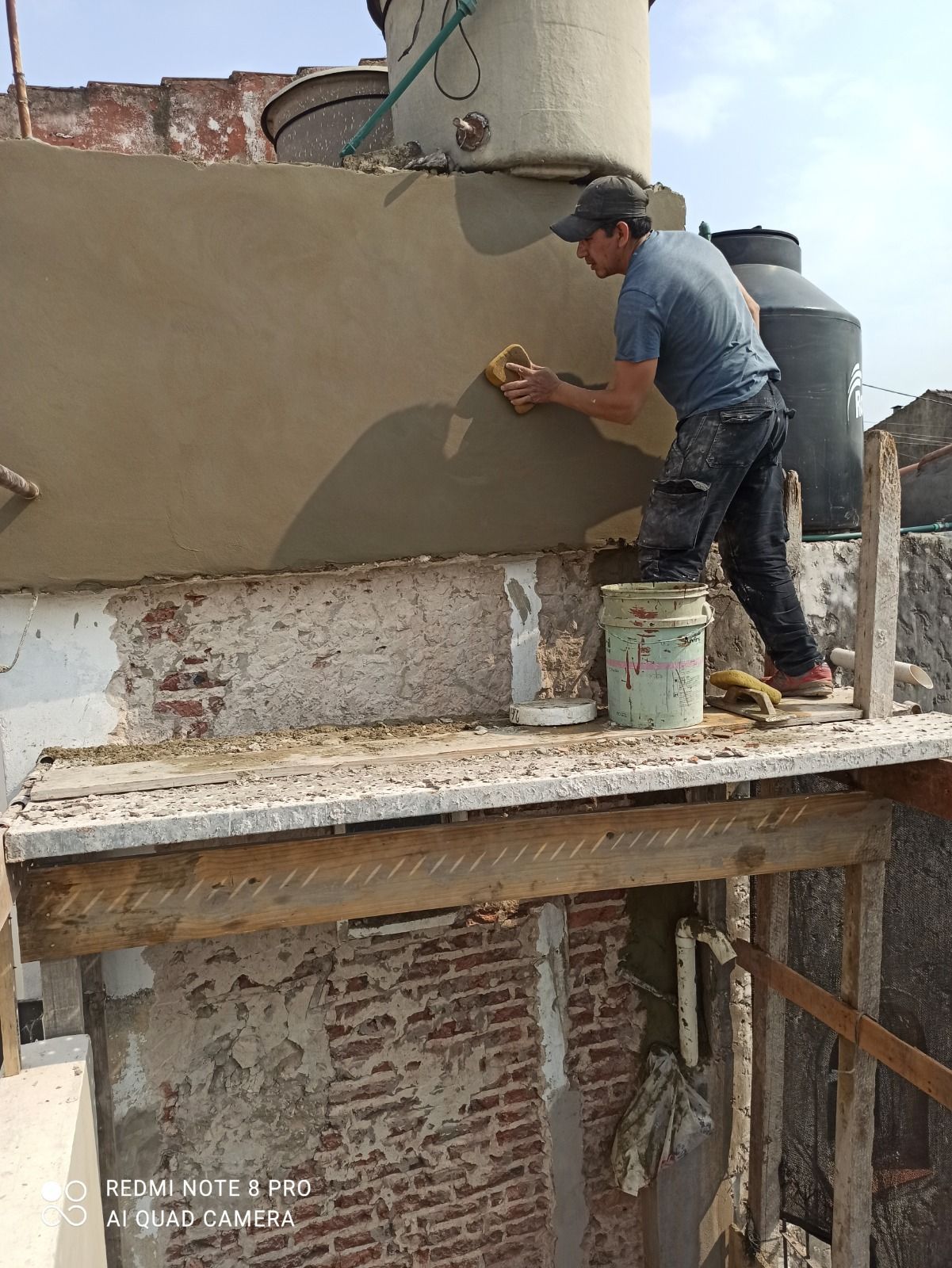 Obrero enyesando una pared exterior en un andamio en la azotea de un edificio.