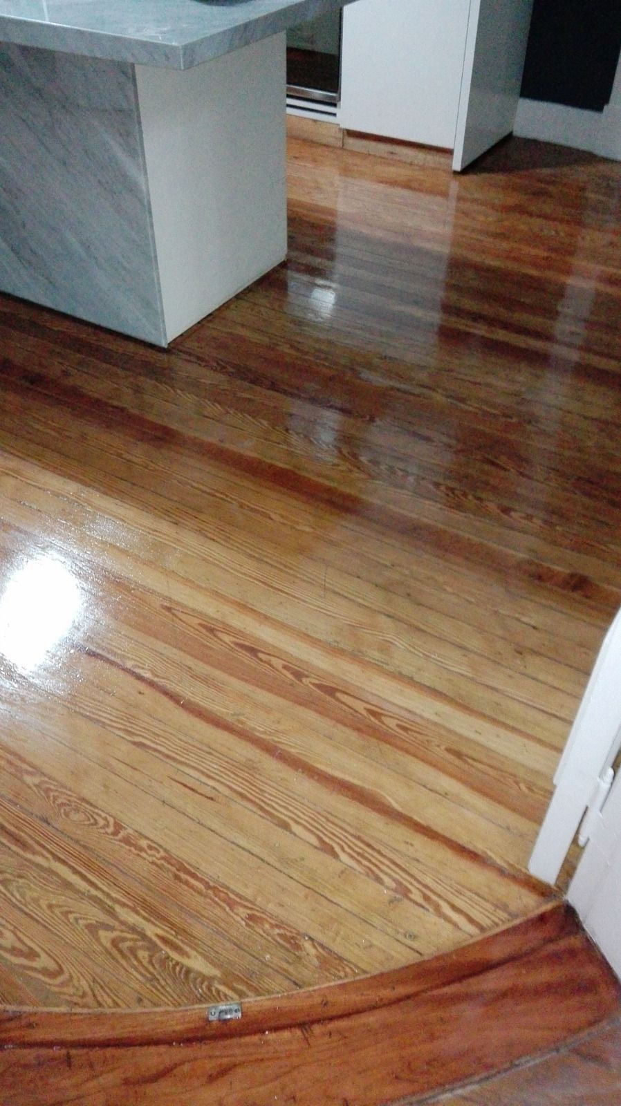 Suelo de madera pulida en una habitación con muebles gris claro y un umbral de madera curvado.