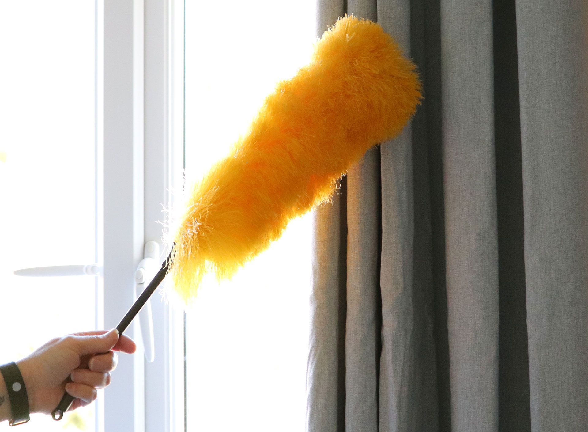 A person is holding a yellow duster in front of a window.
