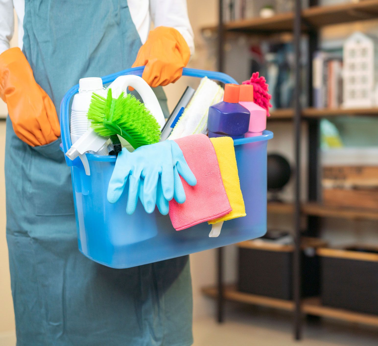 A person is holding a blue bucket filled with cleaning supplies.