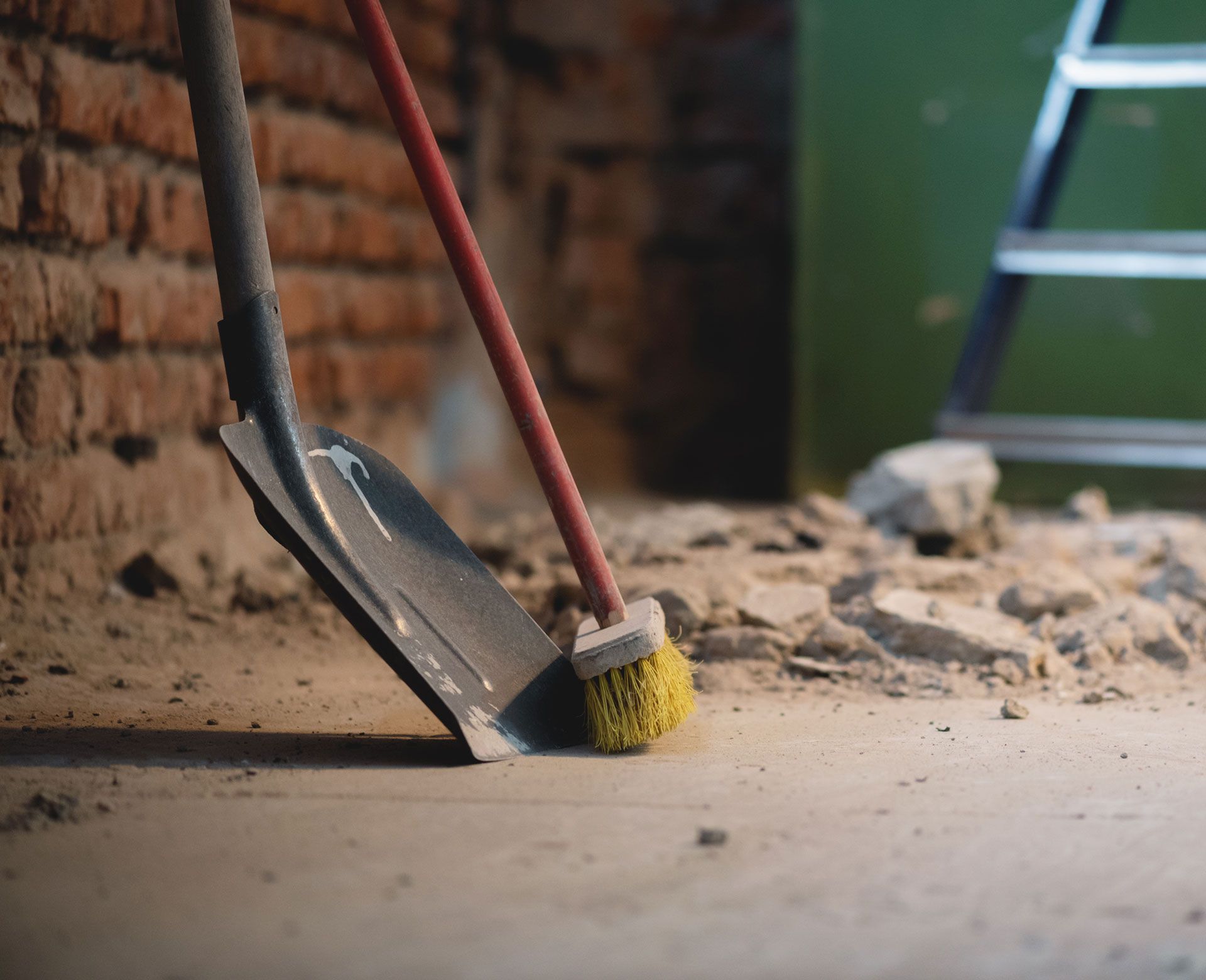 A shovel and a broom are sitting on a dirt floor.