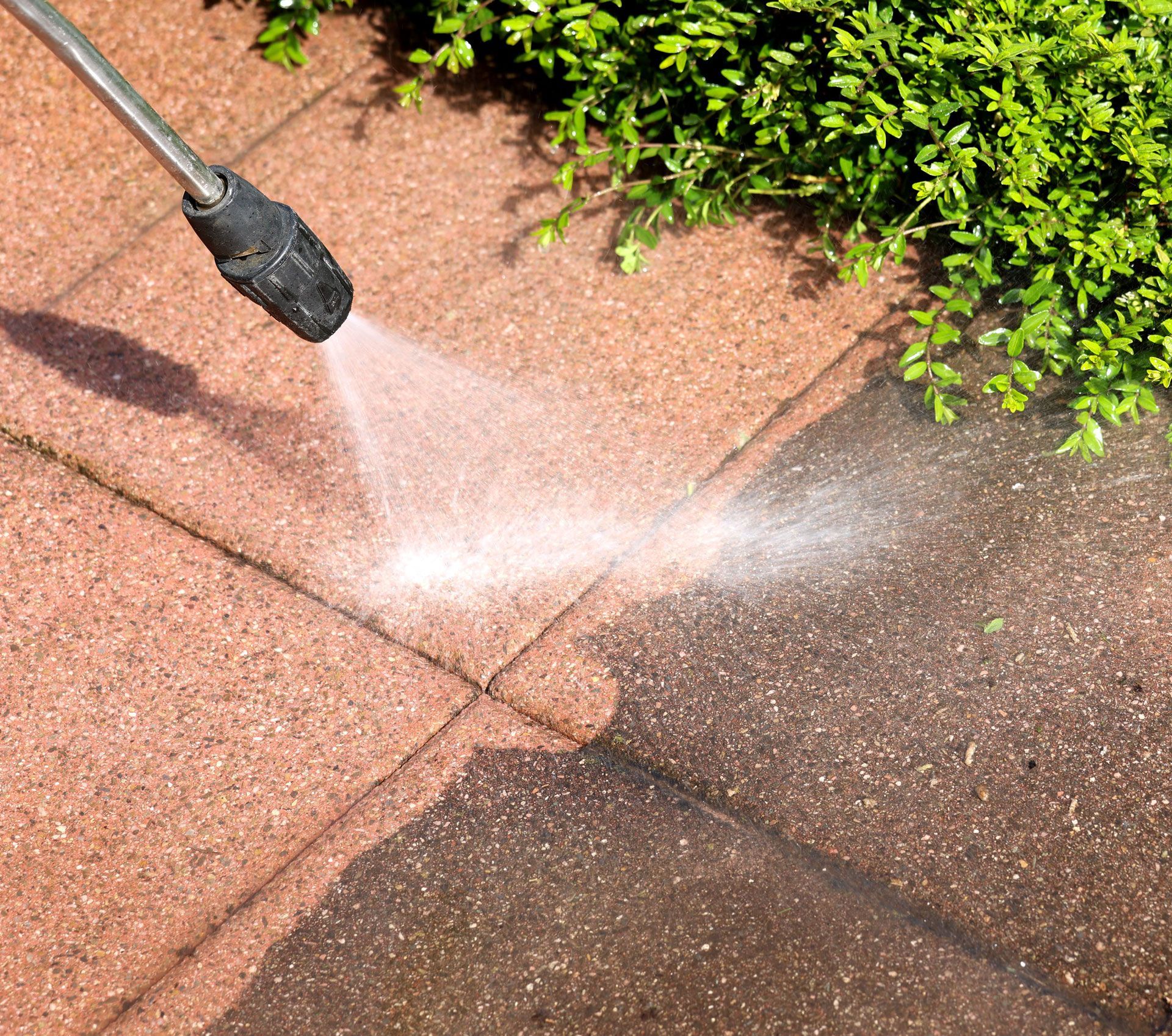 A person is using a high pressure washer to clean a brick walkway.
