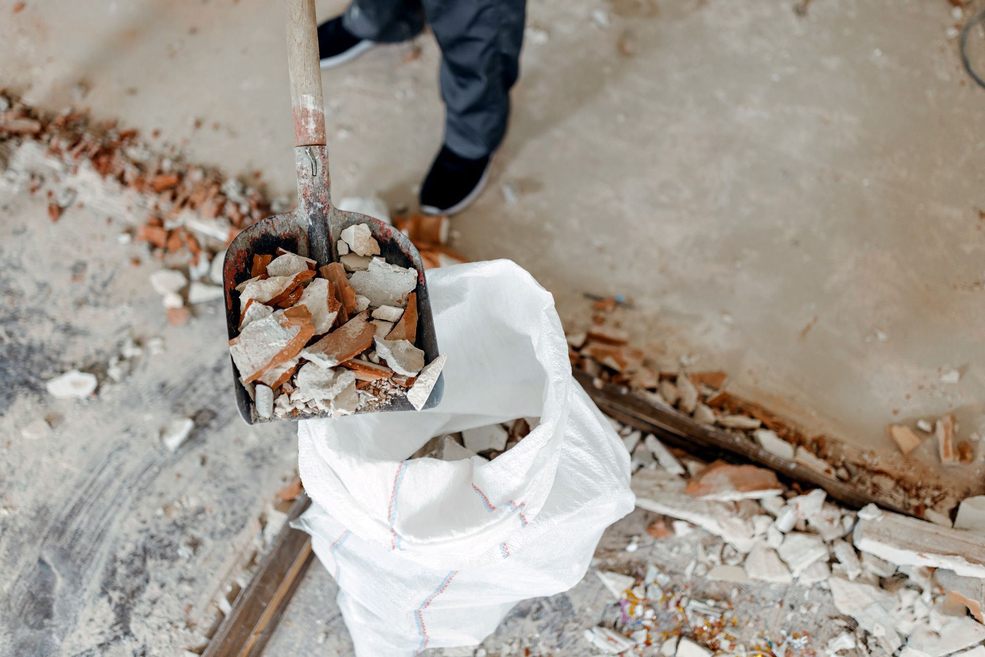 A person is holding a shovel full of bricks and a bag of bricks.