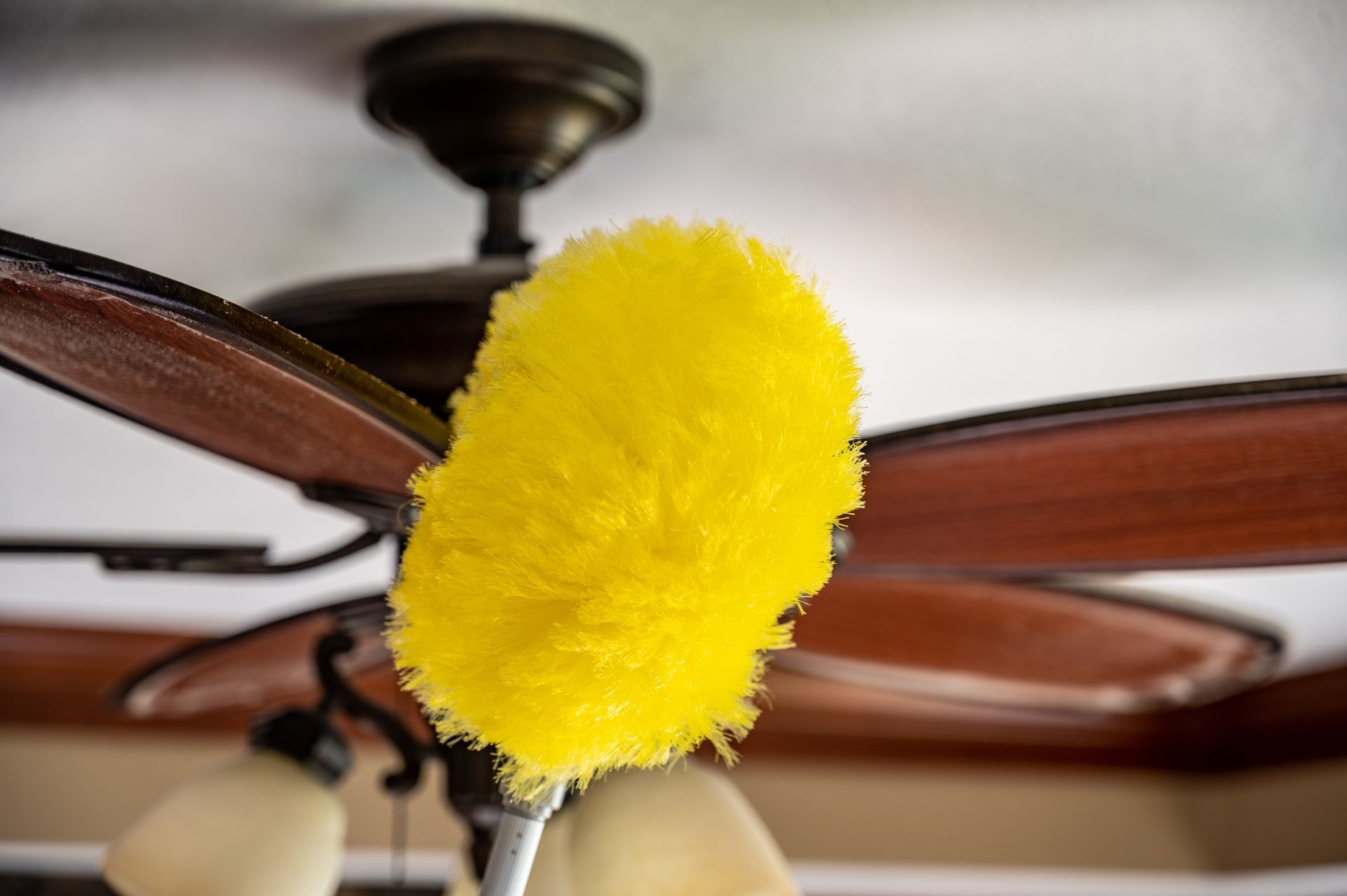 A yellow duster is hanging from a ceiling fan.