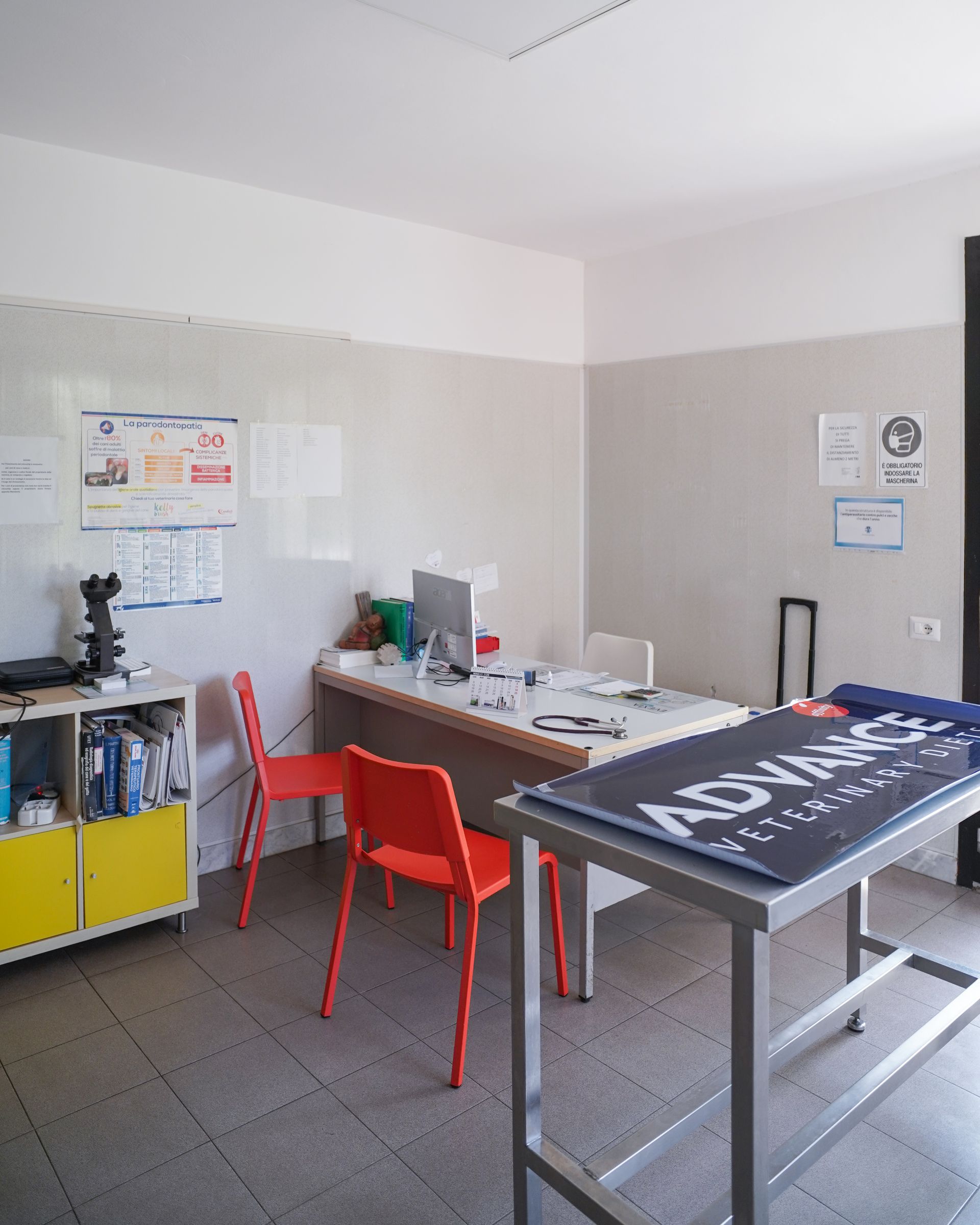 Ufficio con scrivania, sedie rosse e una lavagna bianca. Su un tavolo c'è un cartello con la scritta