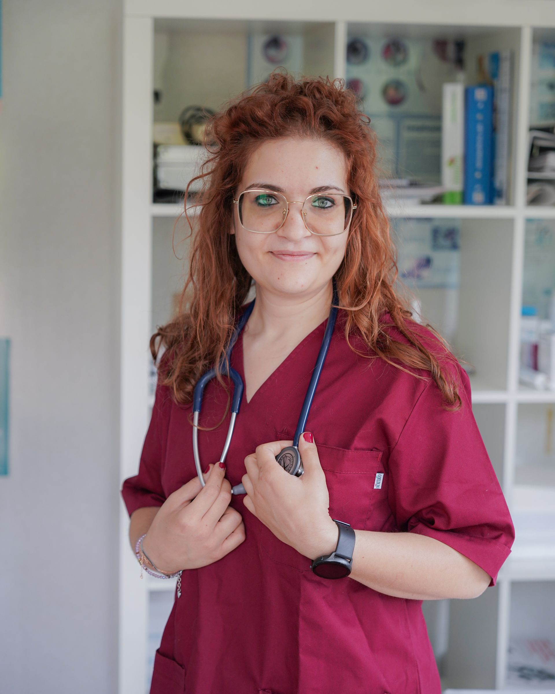 Donna con i capelli rossi, che indossa camice e occhiali, e tiene in mano uno stetoscopio in uno studio medico.