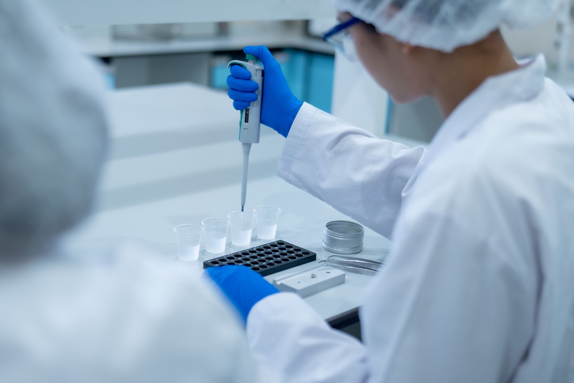 Scienziato in camice e guanti che utilizza una pipetta, mentre lavora con provette in un ambiente sterile.