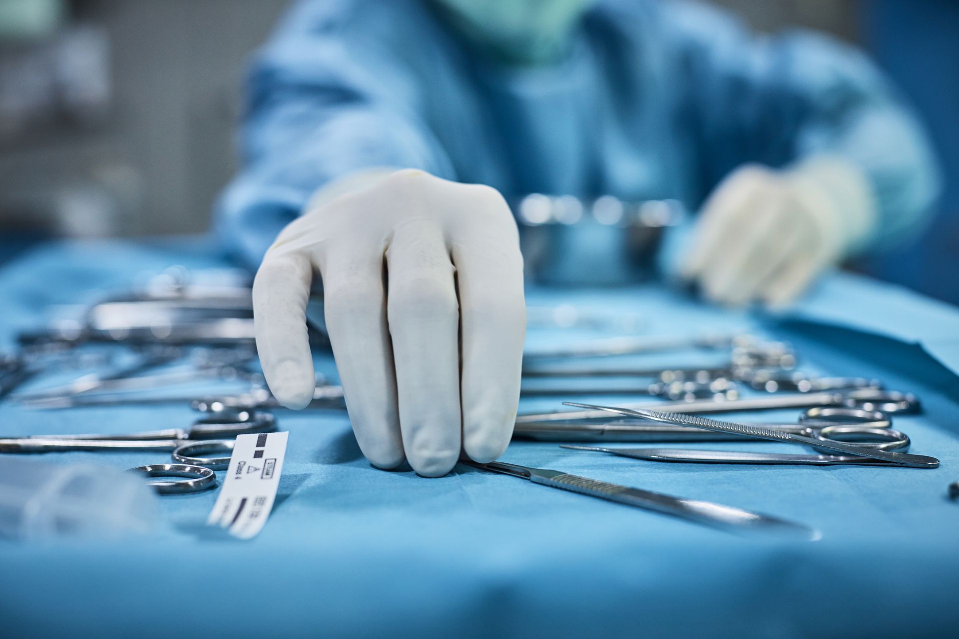 Mano guantata di un chirurgo che prende uno strumento chirurgico su un tavolo blu sterile.