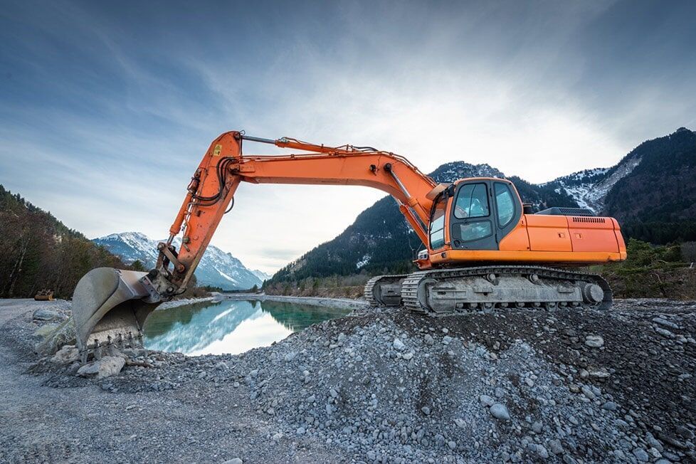 A Large Orange Excavator Is Sitting On Top Of A Rocky Hill Next To A Body Of Water — Kset Engineering in Thornton, NSW