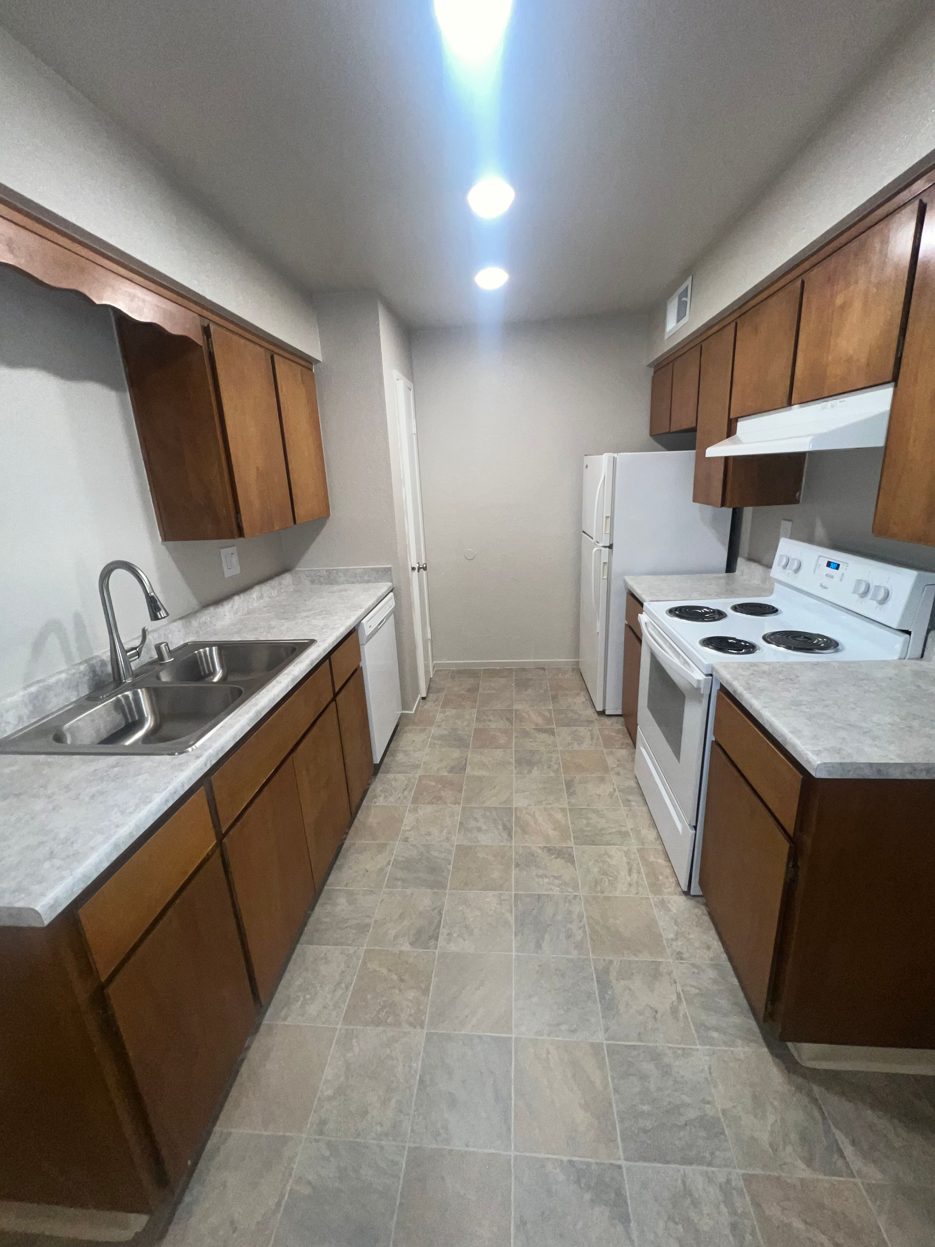 Narrow kitchen with brown cabinets, white appliances, and light countertops.