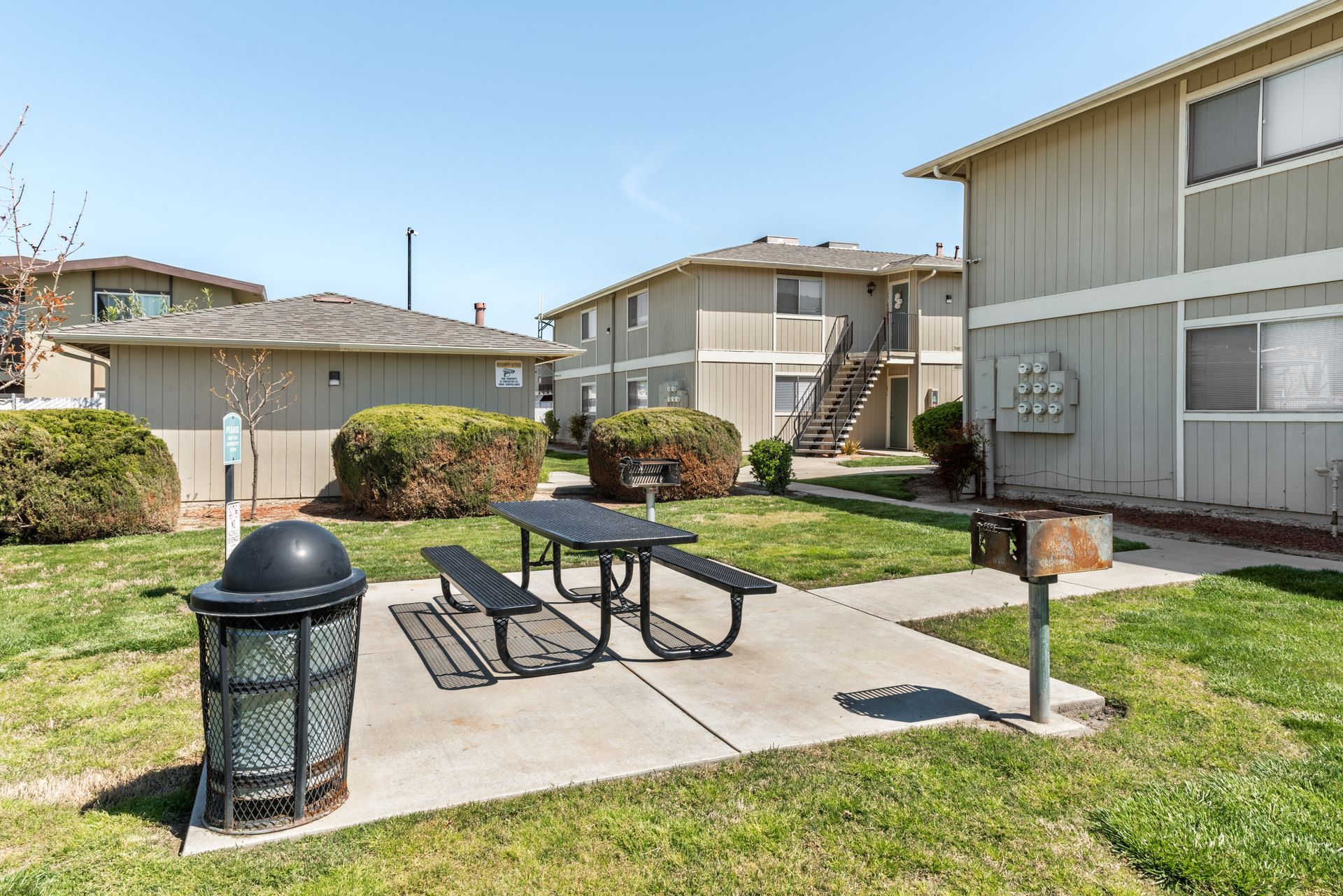 Picnic table and grill outside apartment buildings on a sunny day.
