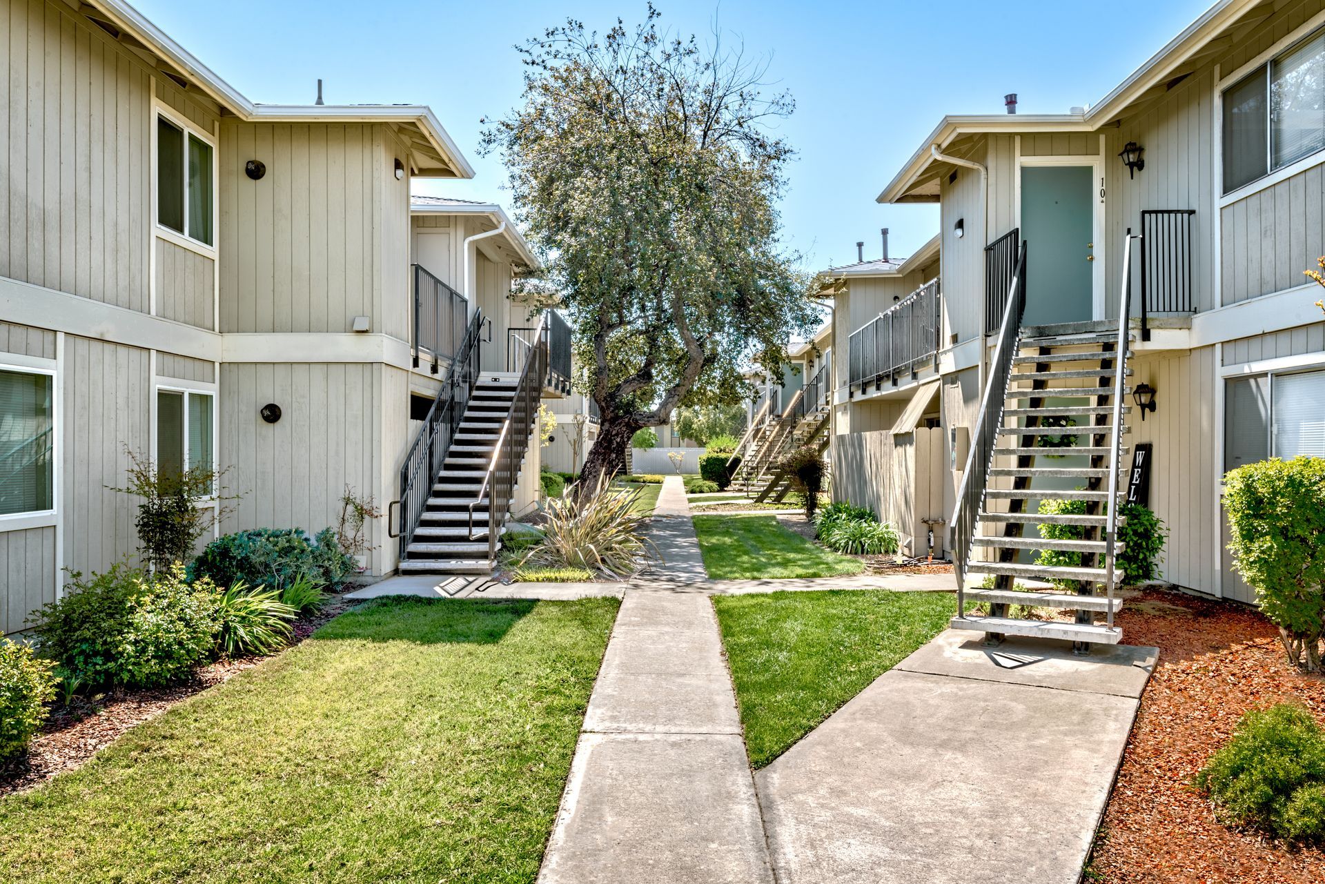 Two-story apartment buildings with exterior staircases on either side of a grassy courtyard.