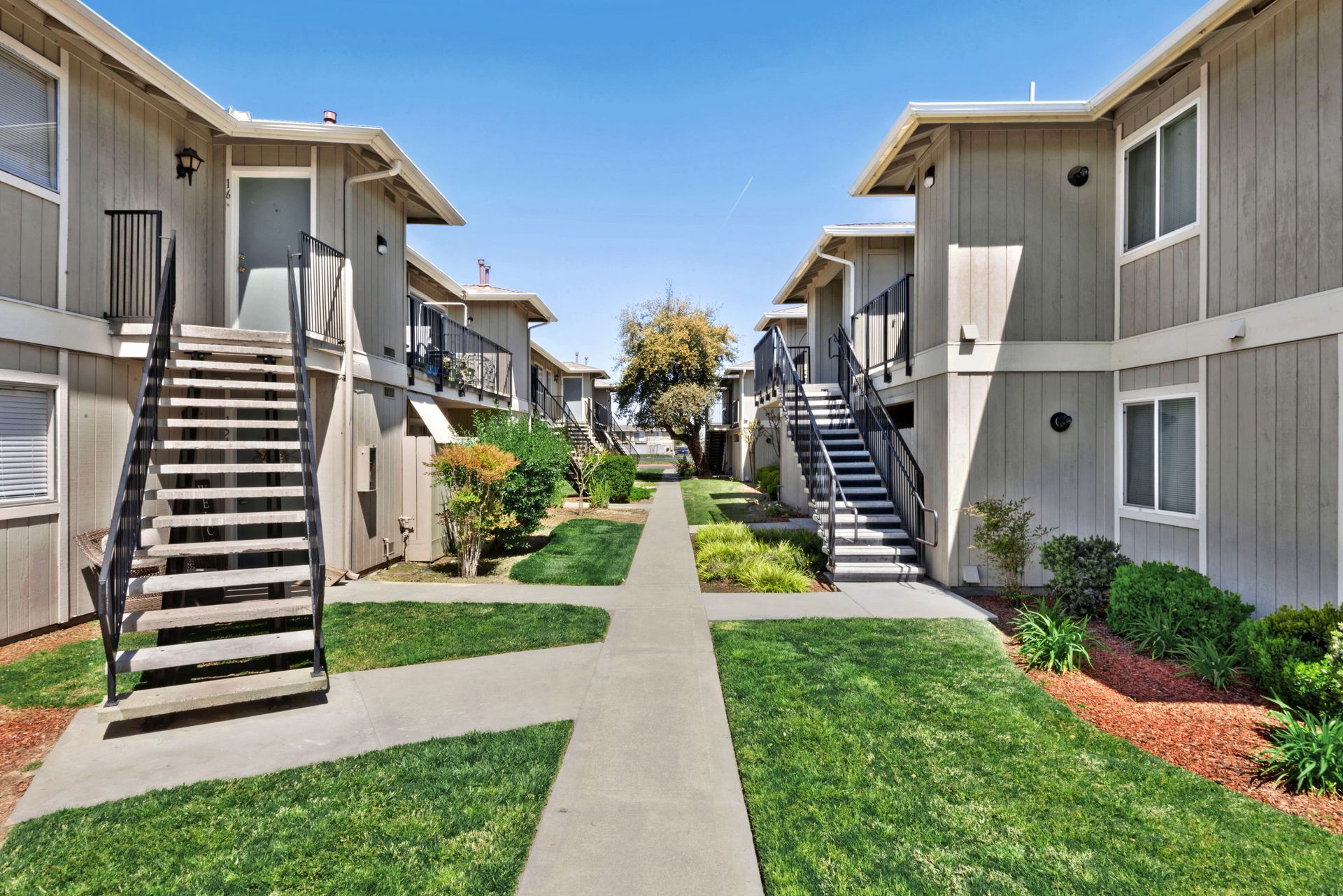 Apartment buildings with exterior staircases and a central walkway, grass, and blue sky.