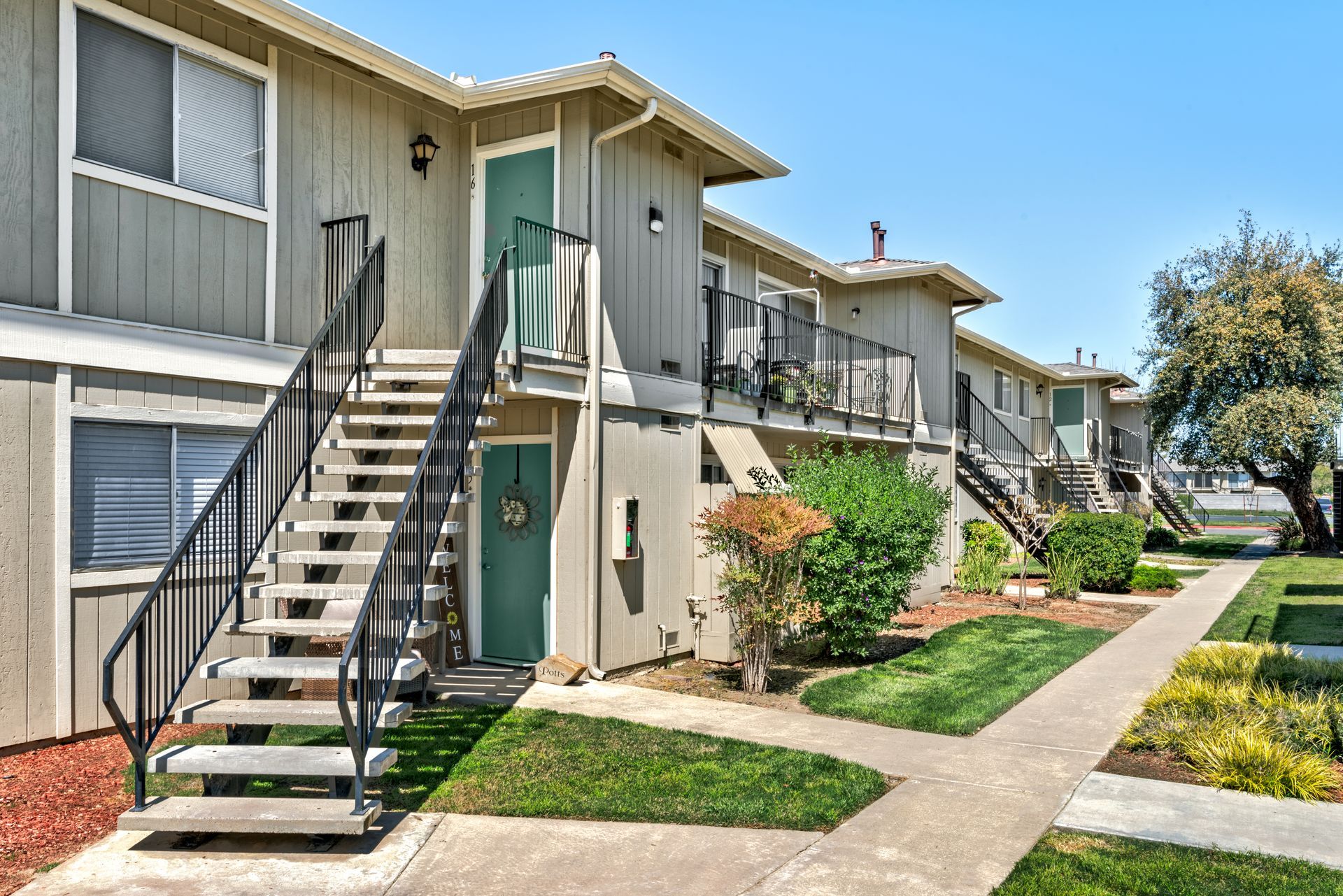 Apartment complex with outdoor stairs, green doors, and walkways, under a blue sky.