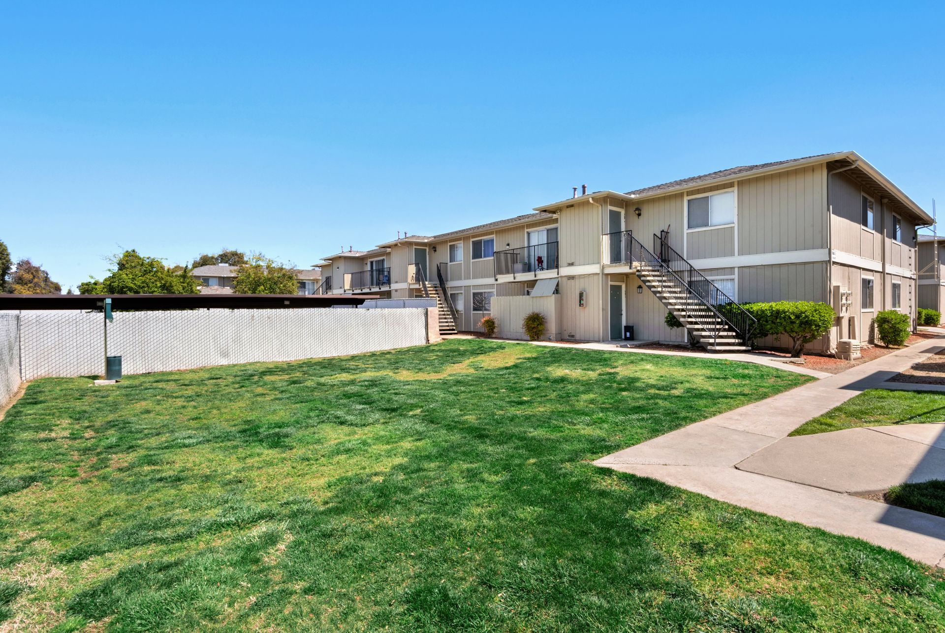 Apartment building with green lawn and white fence under a blue sky.