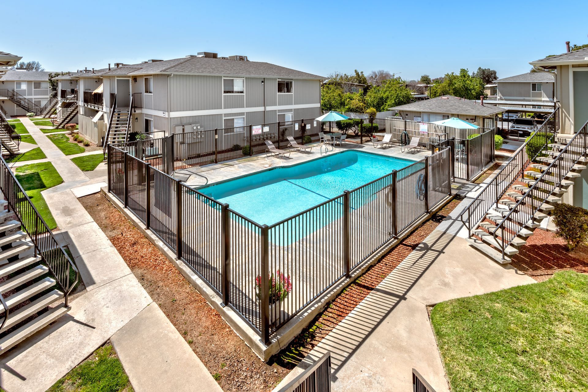 Apartment complex with a fenced swimming pool; blue water, gray buildings, sunny day.