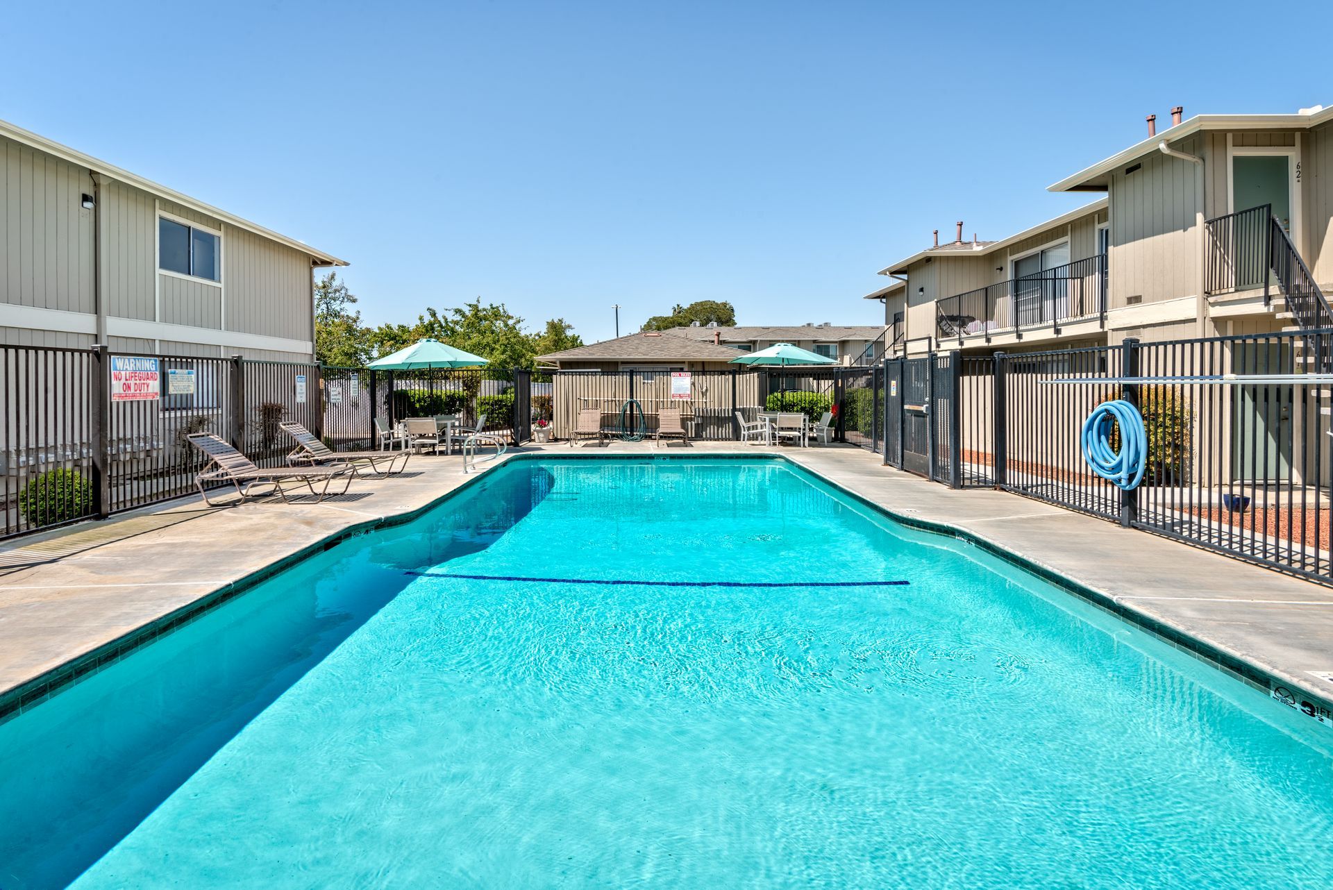Pool between beige apartment buildings under a blue sky.