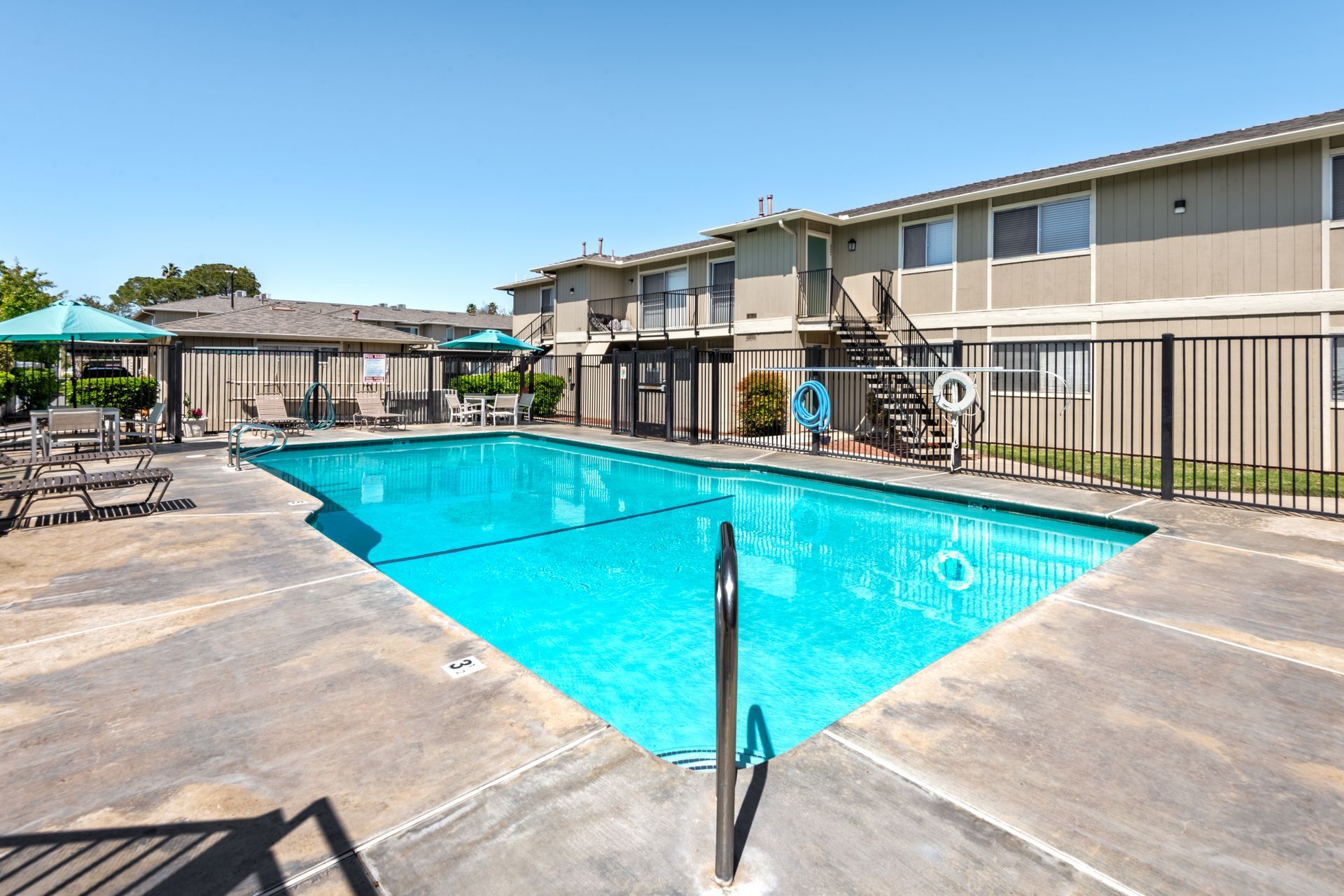 Swimming pool in front of a two-story apartment building on a sunny day.