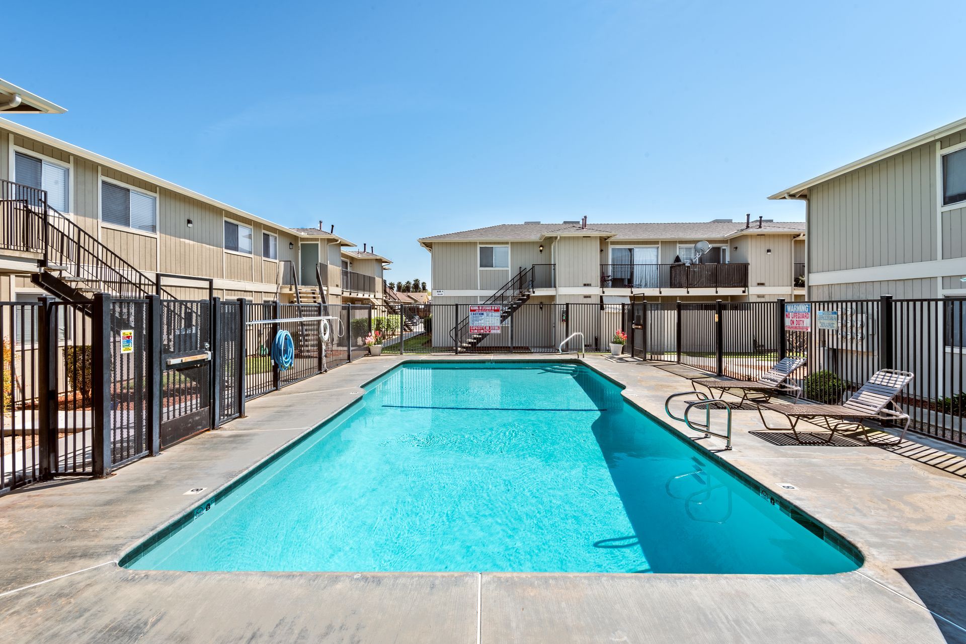 Apartment complex with a swimming pool; buildings are tan, pool is blue; sunny day.