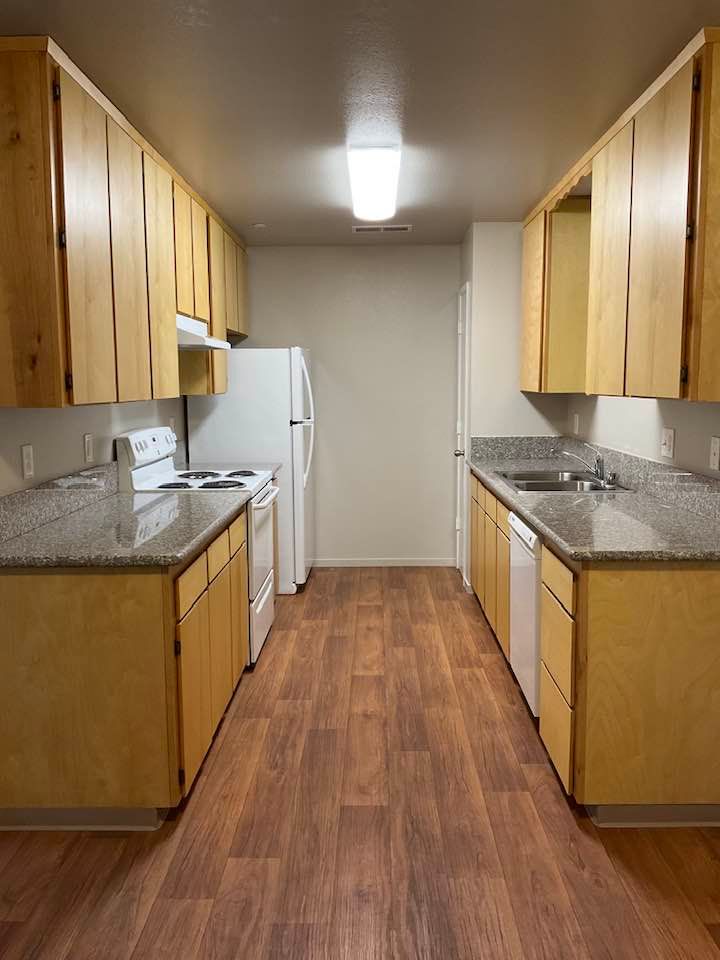 Narrow kitchen with wood cabinets, granite counters, and appliances; wood-look floor.