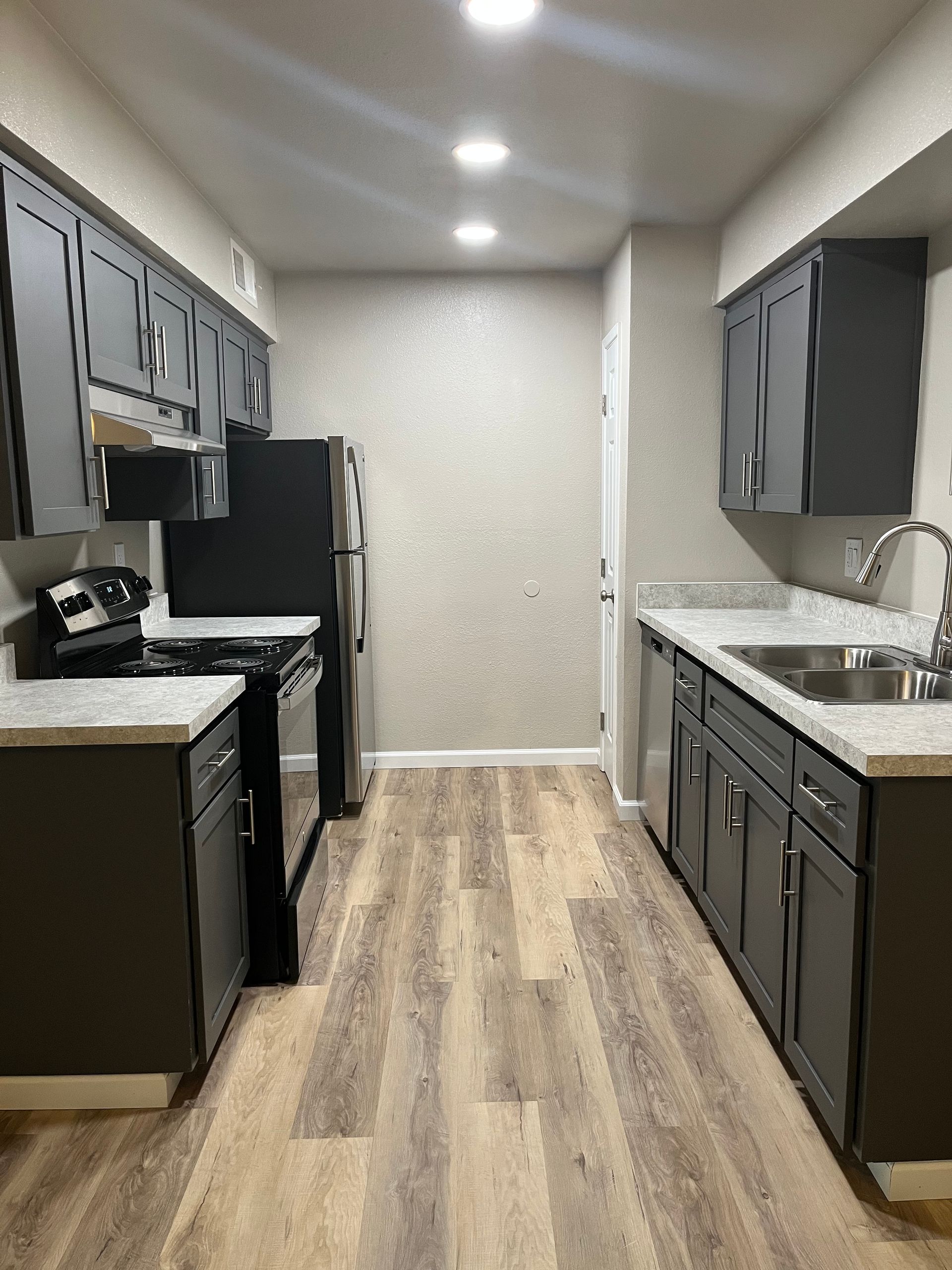 Modern kitchen with gray cabinets, stainless steel appliances, and wood-look floors.