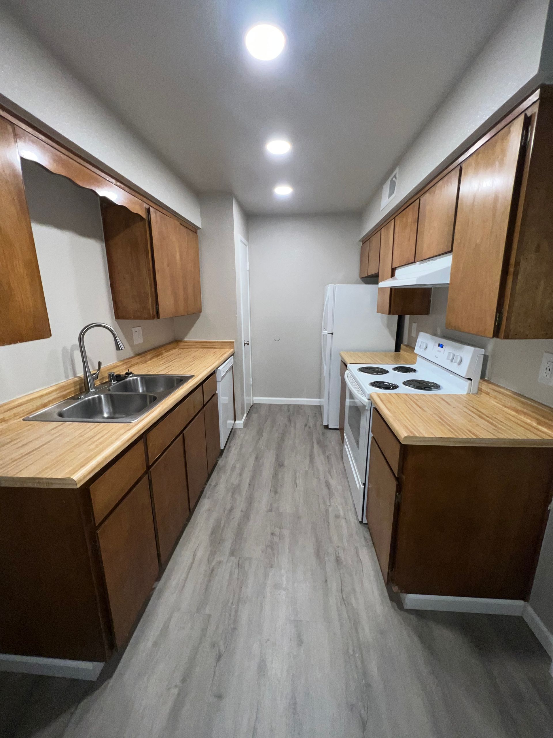 Narrow kitchen with wood cabinets, light countertops, and gray flooring.
