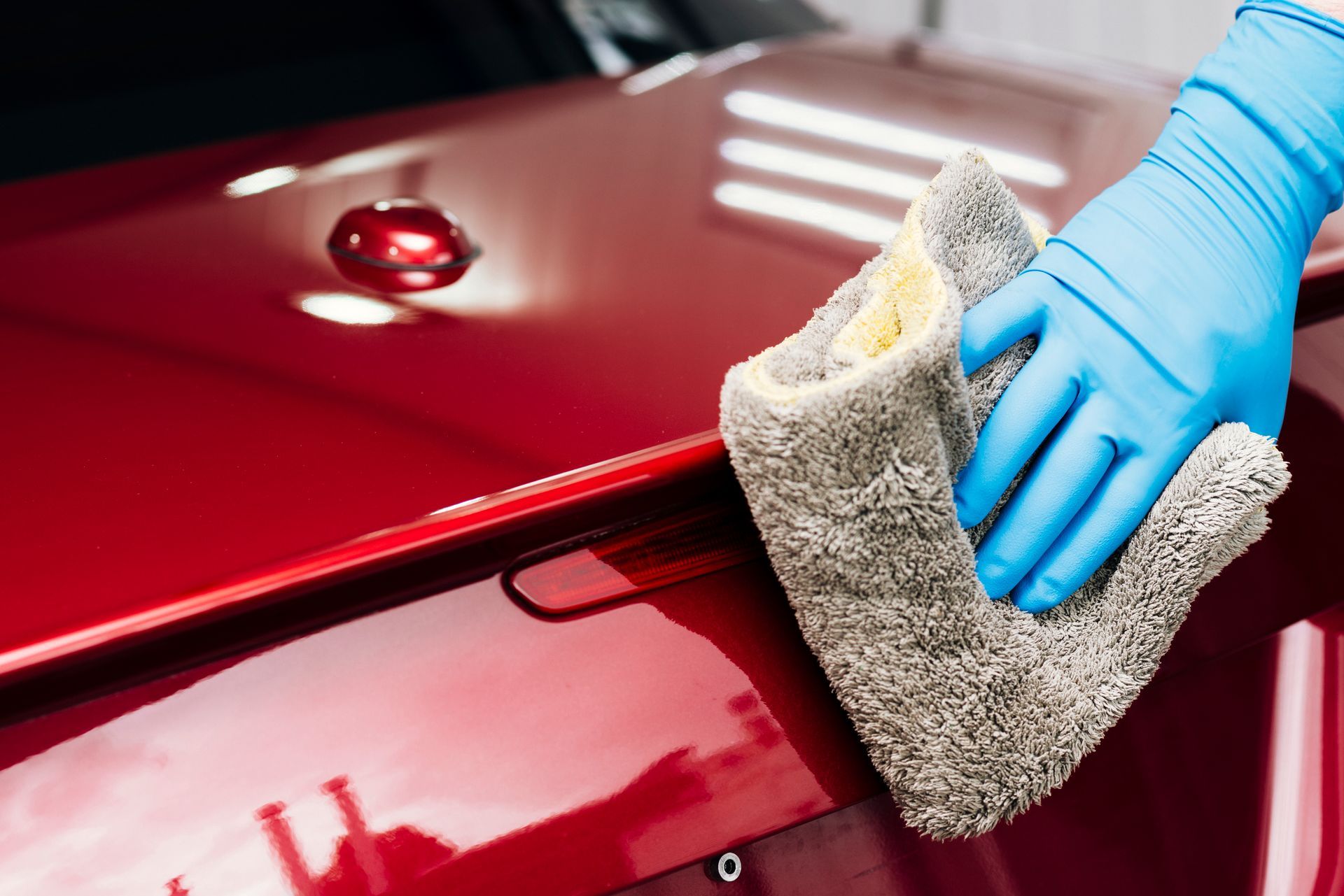 Blue-gloved hand polishing a red car with a gray cloth