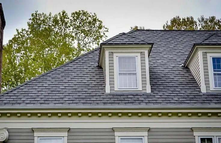 A close-up of a house featuring gray shingles and two white dormer windows.