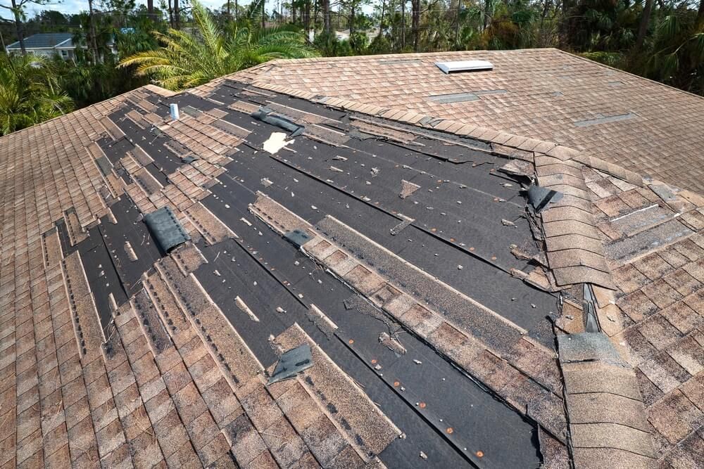 Wind-damaged roof with missing asphalt shingles after hurricane