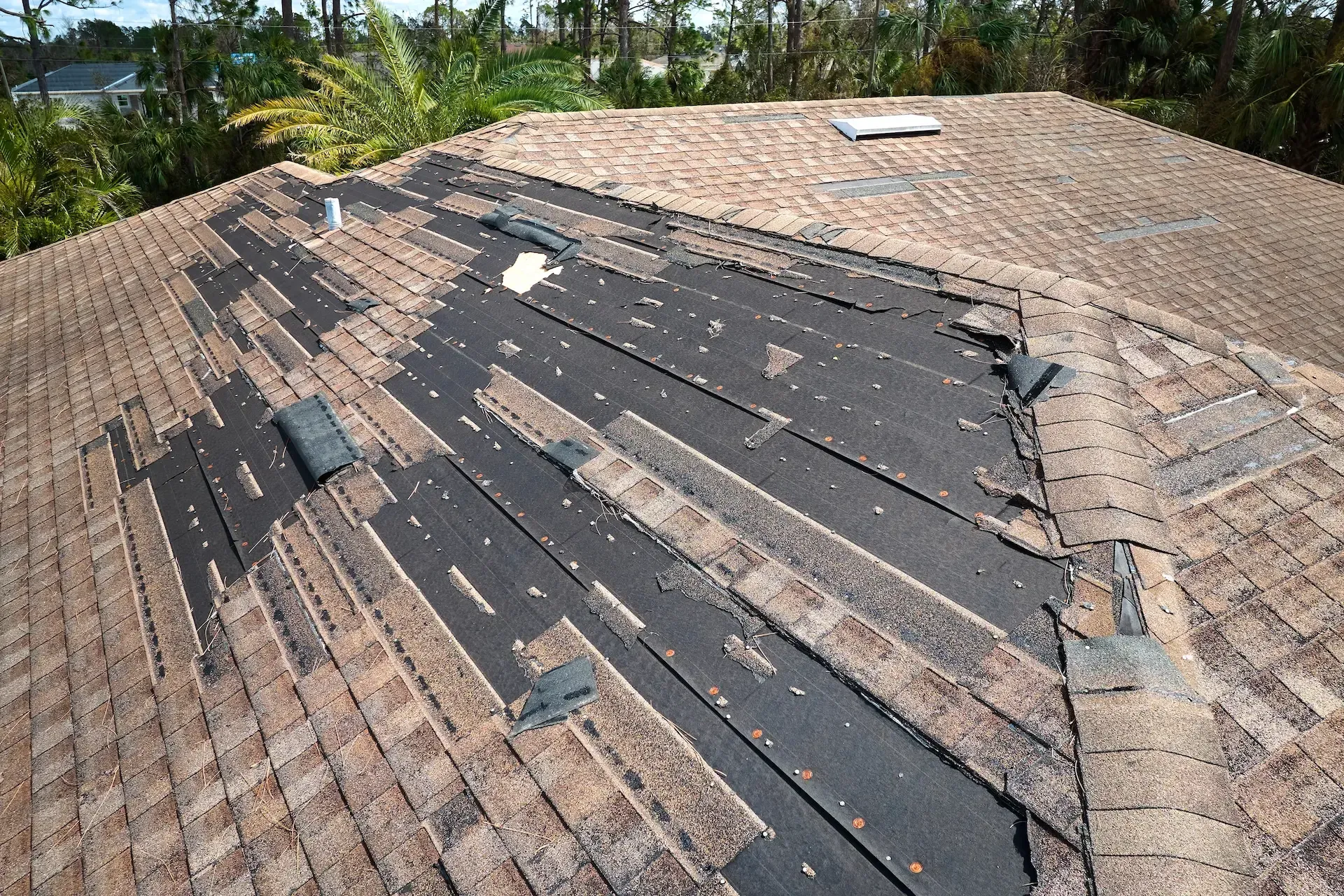 Wind damaged house roof with missing asphalt shingles after hurricane 