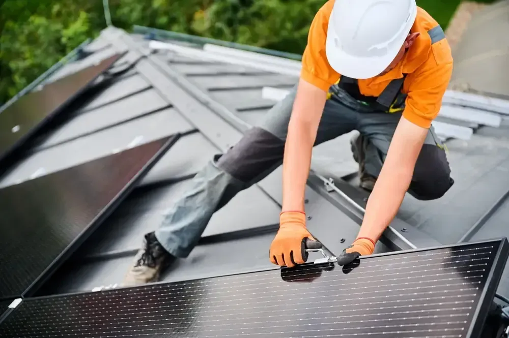 Man engineer in helmets and gloves installing solar module with help of hex key outdoors.