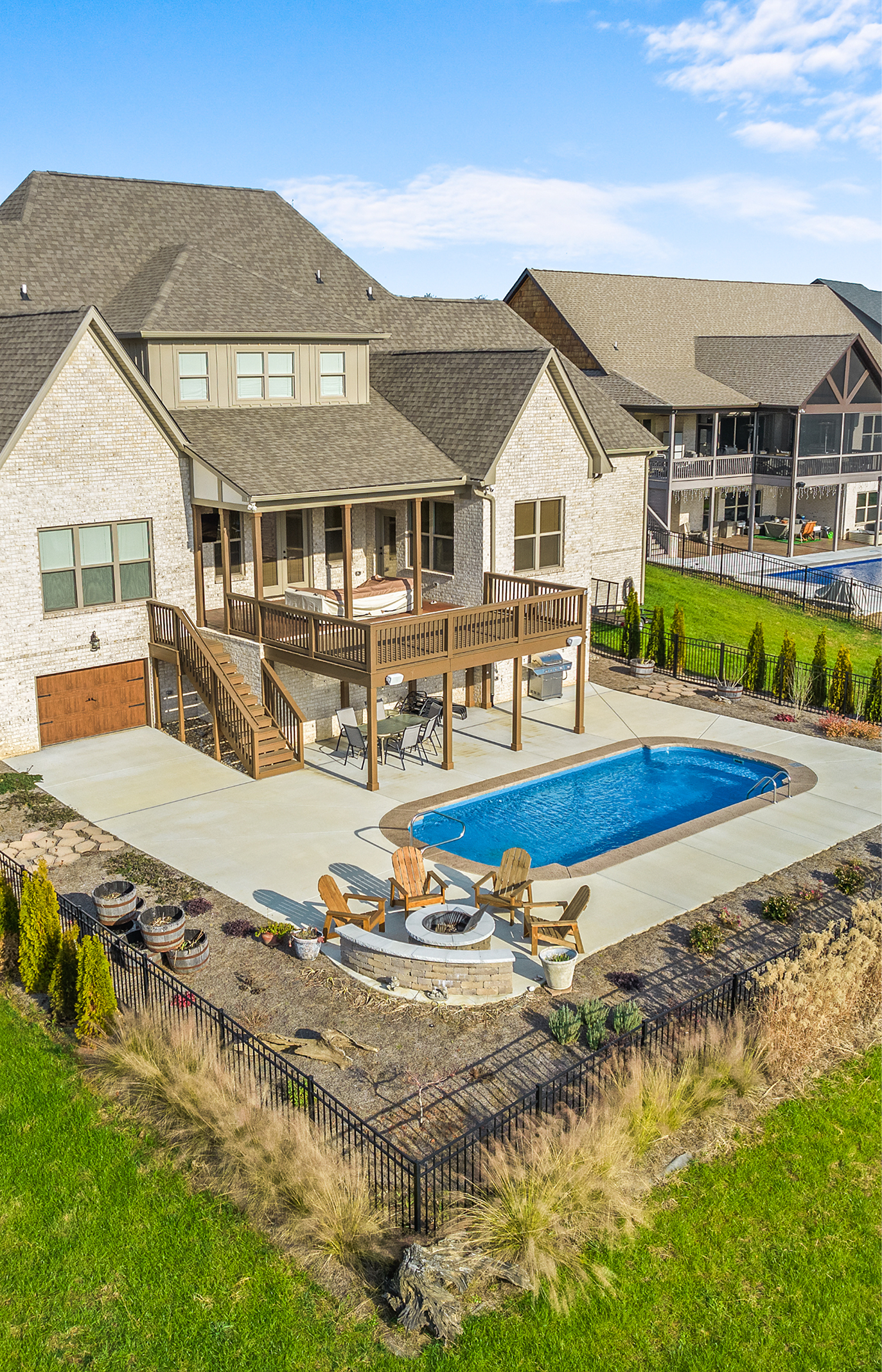 Backyard with a pool, deck, and fire pit in front of a stone house with a multi-level roof.