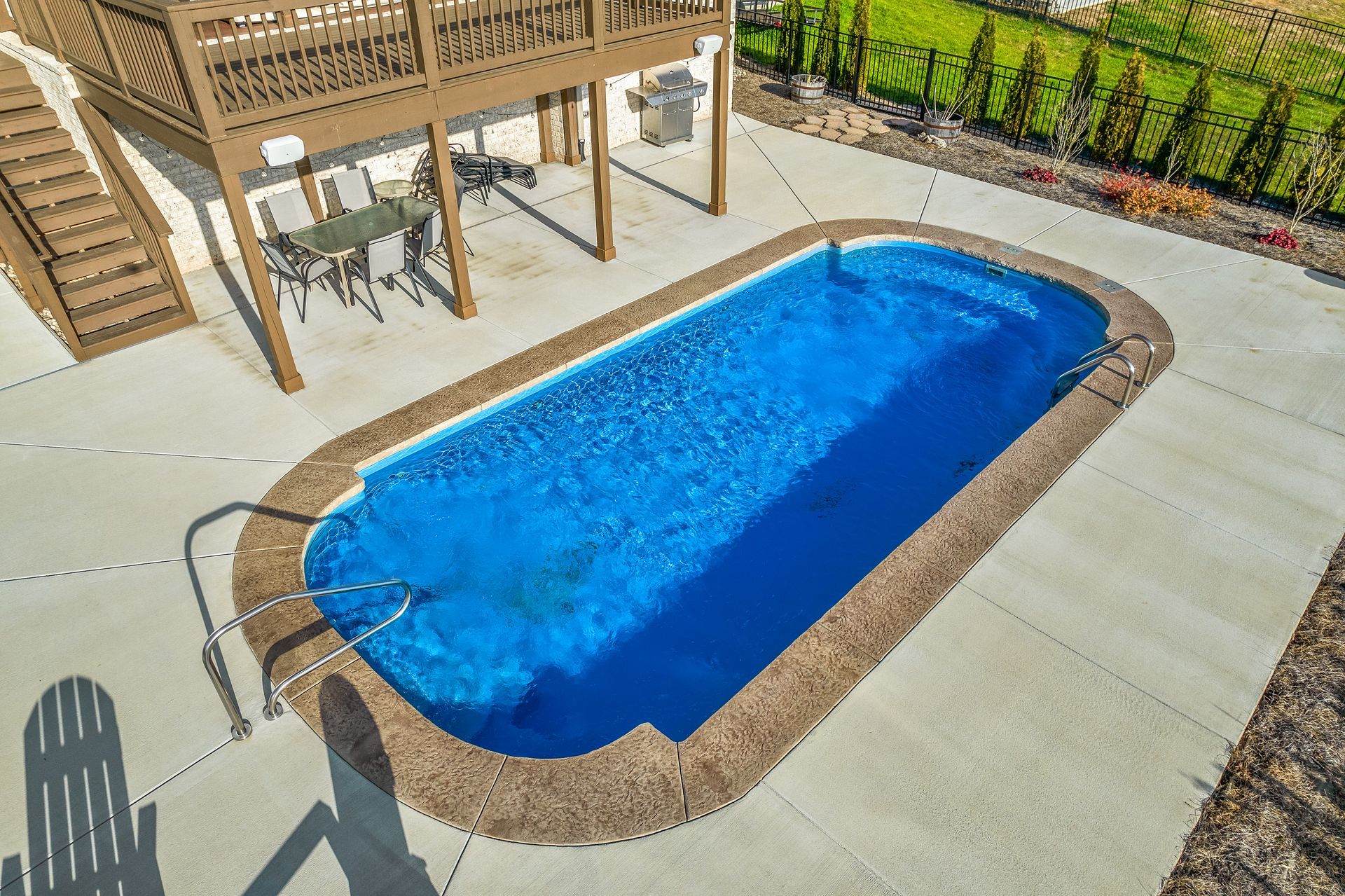 Overhead view of a rectangular pool with blue water. A deck with stairs is to the left, and concrete surrounds the pool.