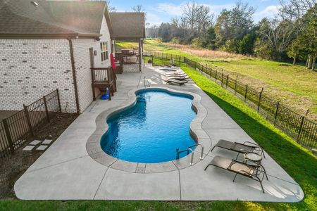 Aerial view of a rectangular blue swimming pool with brown bordering, surrounded by concrete and a wooden deck.
