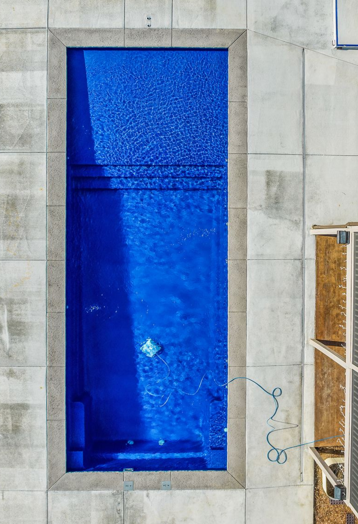 Rectangular pool with turquoise water, surrounded by wooden decking and three striped lounge chairs.
