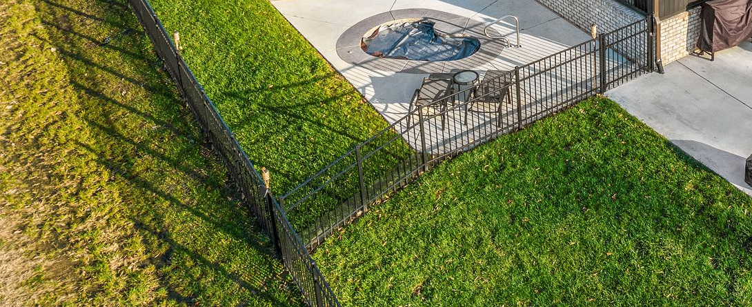 Pool surrounded by a flower garden with irrigation tubing. Stone patio in the foreground, houses in the background.