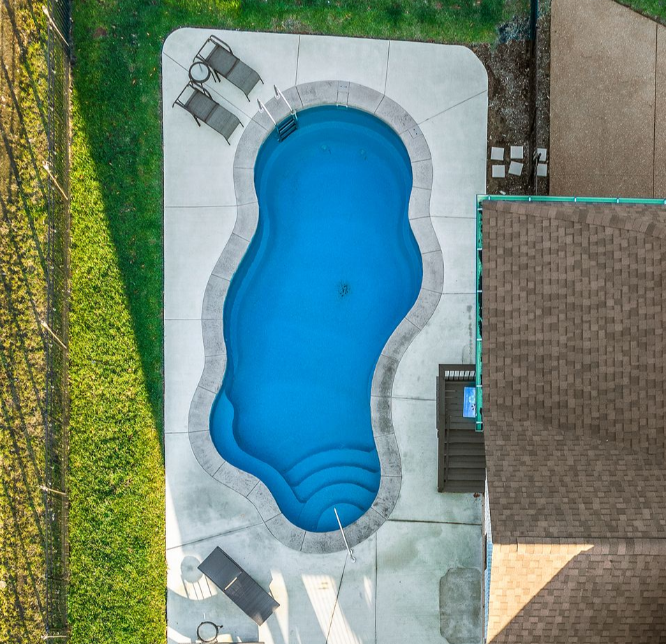 Swimming pool with blue water and concrete patio, with construction site in the background under a blue sky.