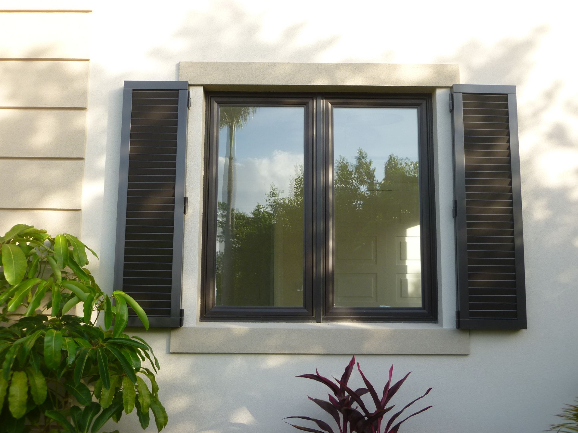 A window with black shutters on a white wall