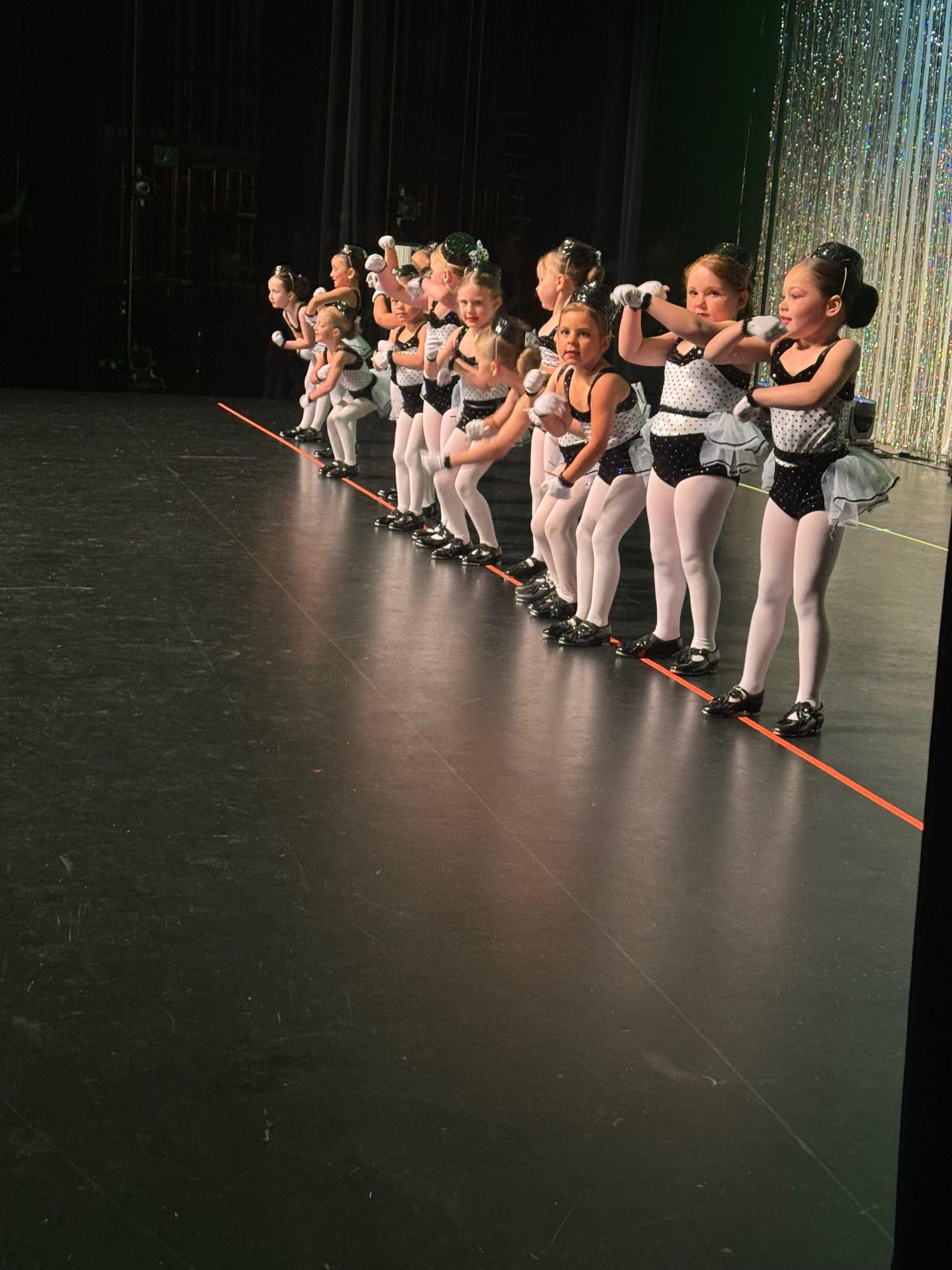 A group of young ballerinas are standing on a stage.