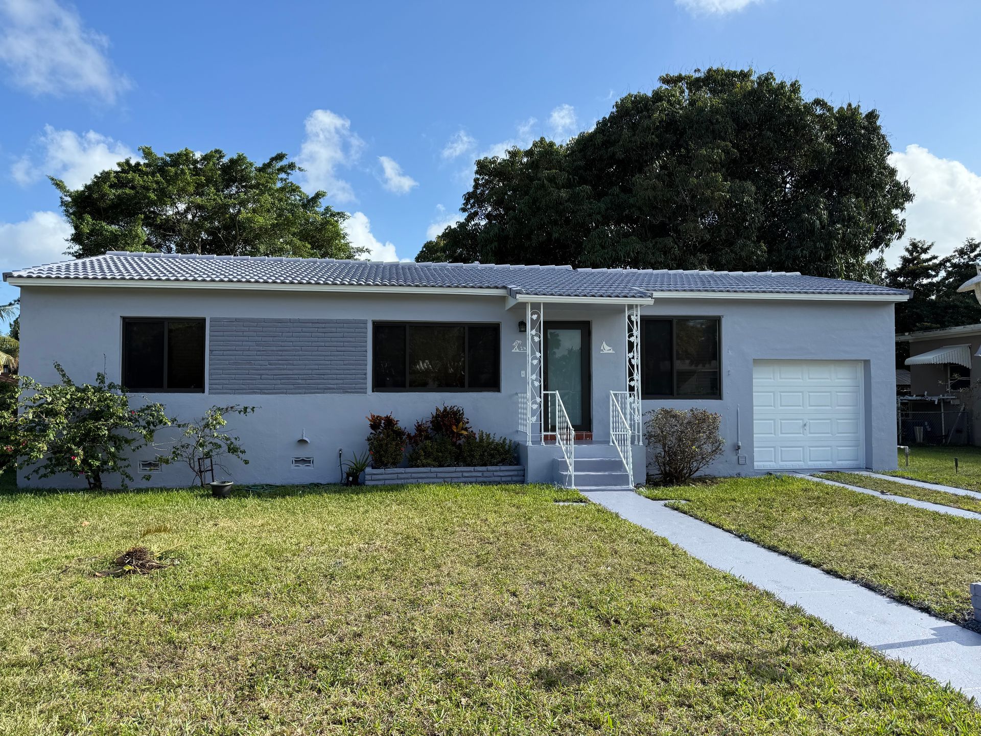 Light blue ranch house with a gray roof and a concrete walkway. Green lawn and a blue sky.