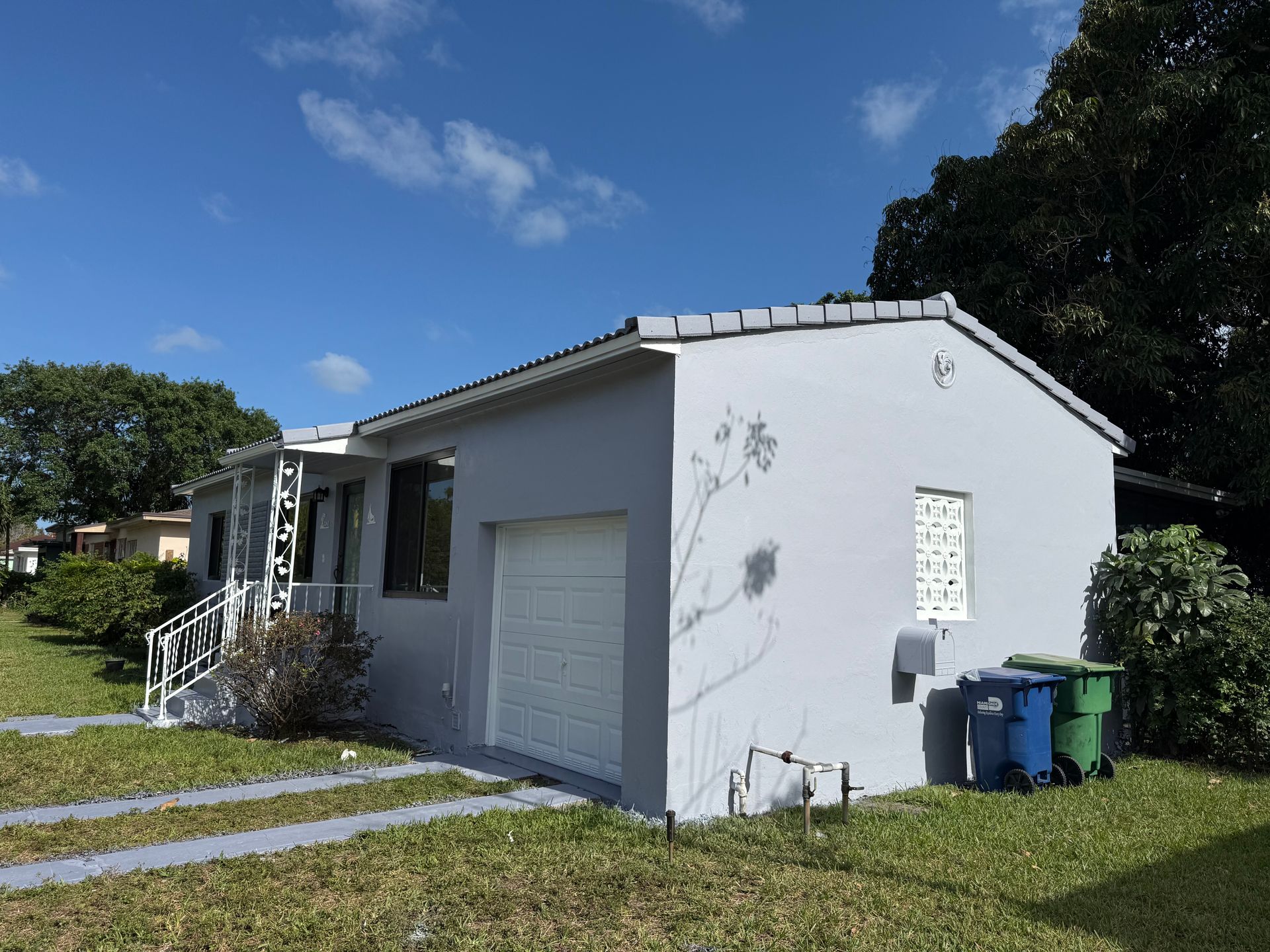 Gray house with white garage door and blue recycling bins on a sunny day.