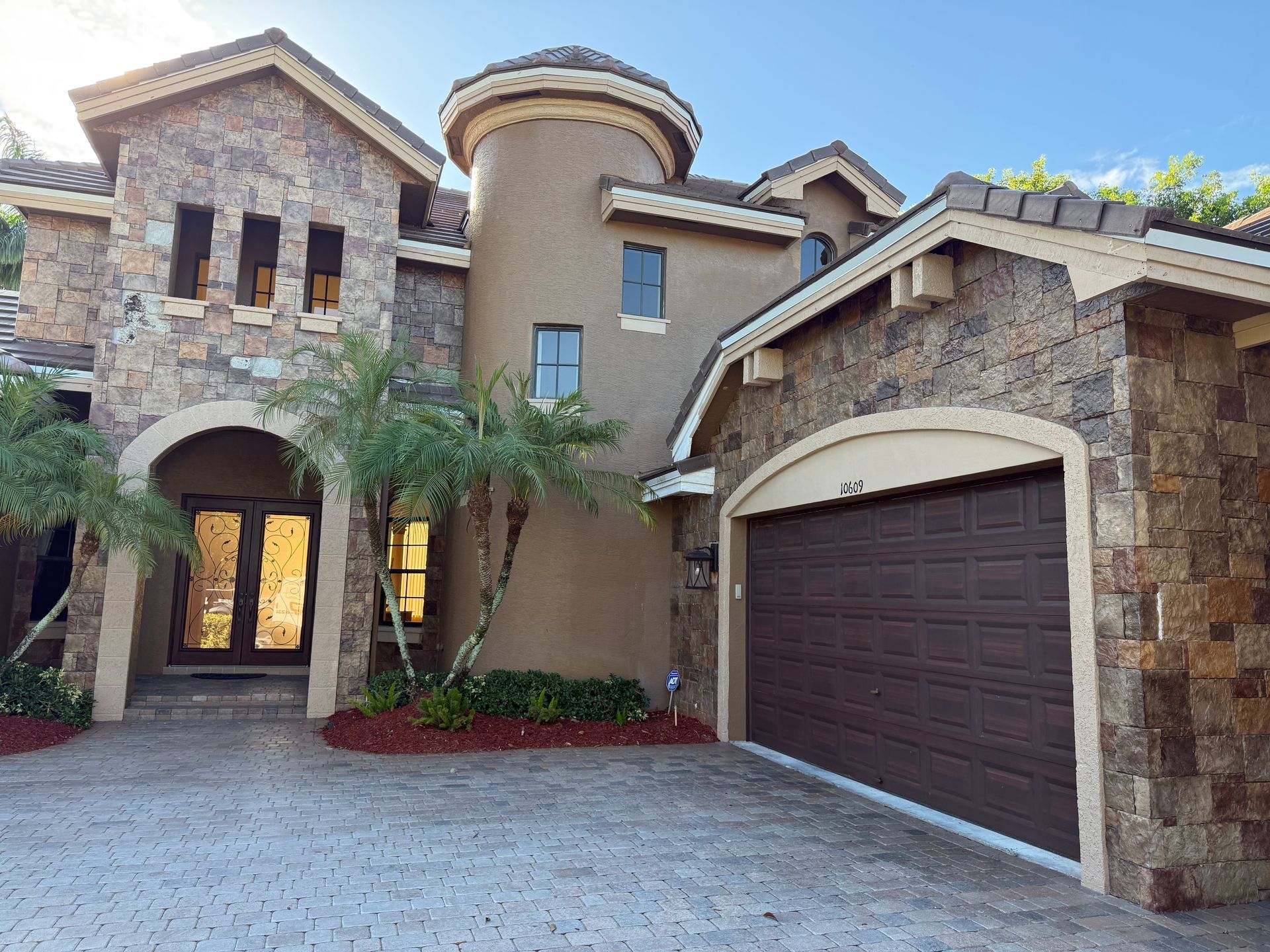 Stone facade luxury home with arched entry, circular tower, and attached garage.