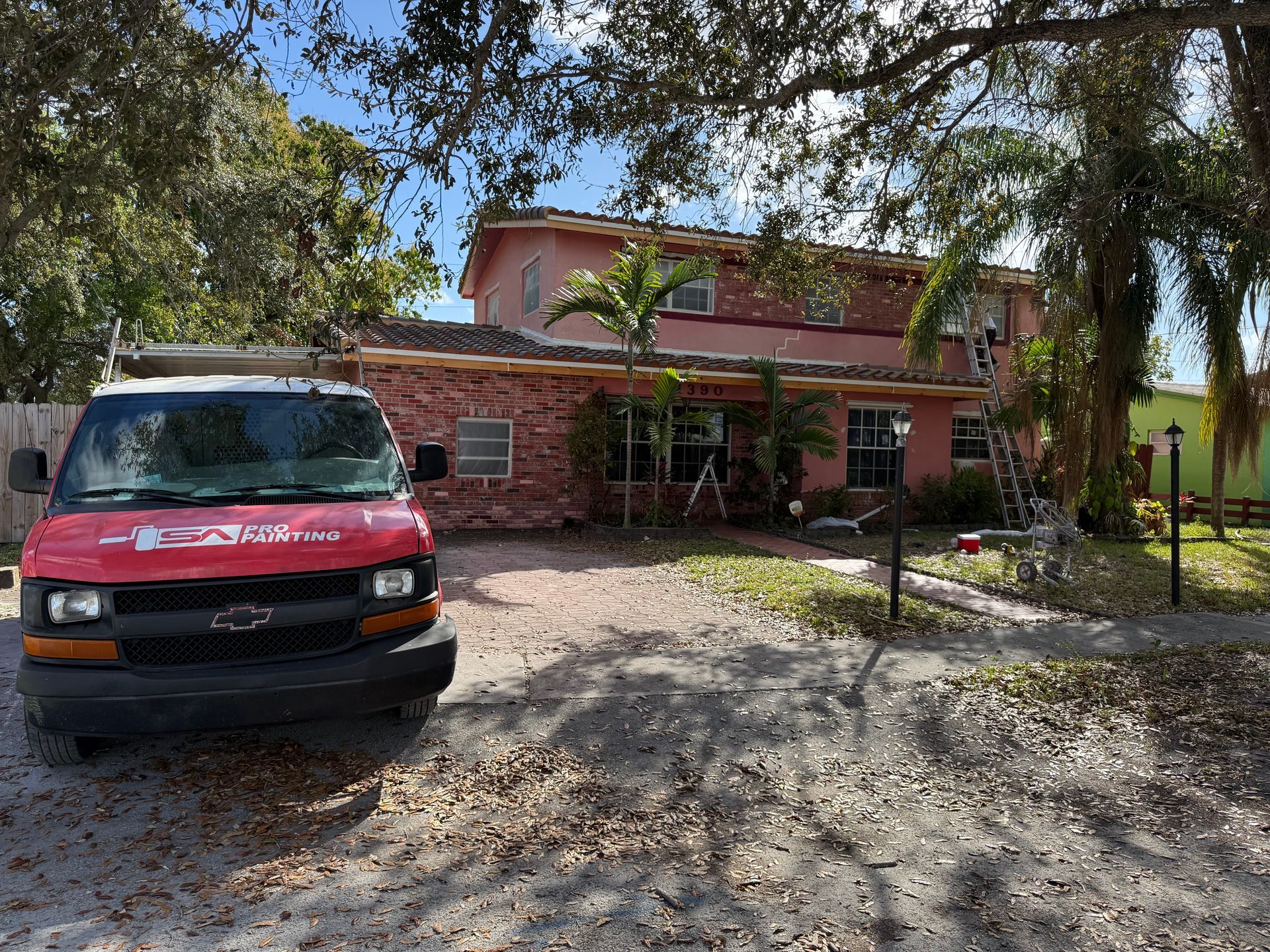 Red van parked in front of a two-story brick house with a ladder leaning against the side.