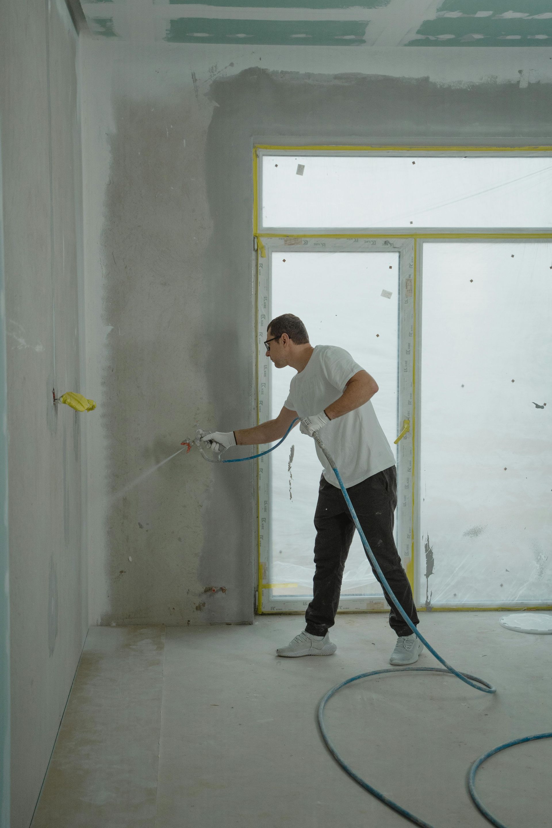 Man spraying plaster on a wall inside a building. He wears gloves and safety glasses.