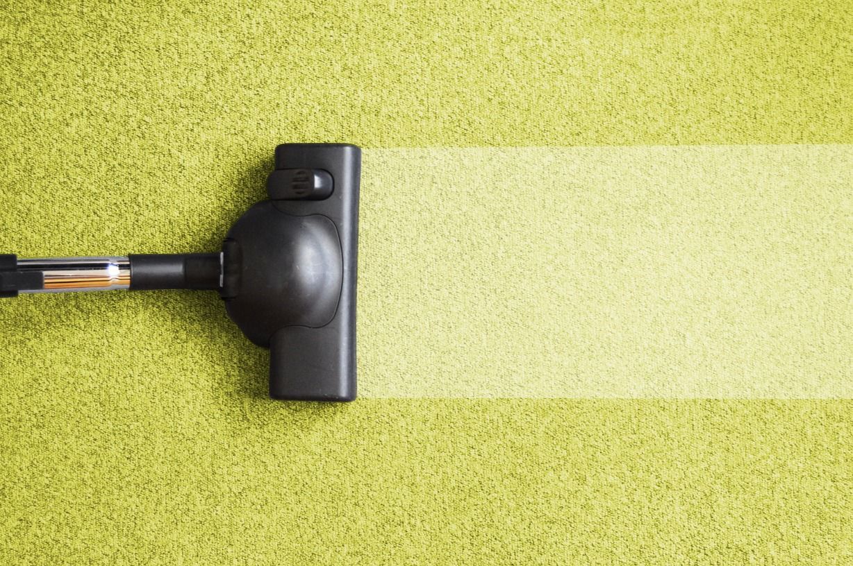 A vacuum cleaner is cleaning a green carpet.