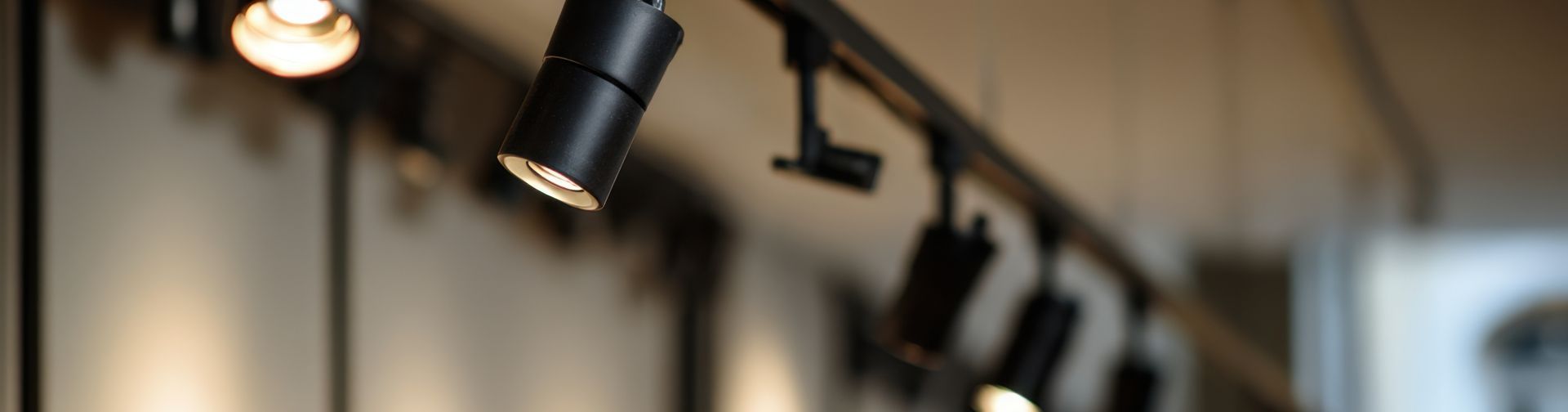 Black track lighting fixtures on a ceiling, blurred background.