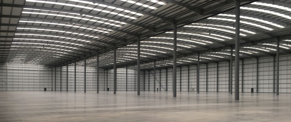 Interior of a large, empty warehouse with metal roof and support columns.