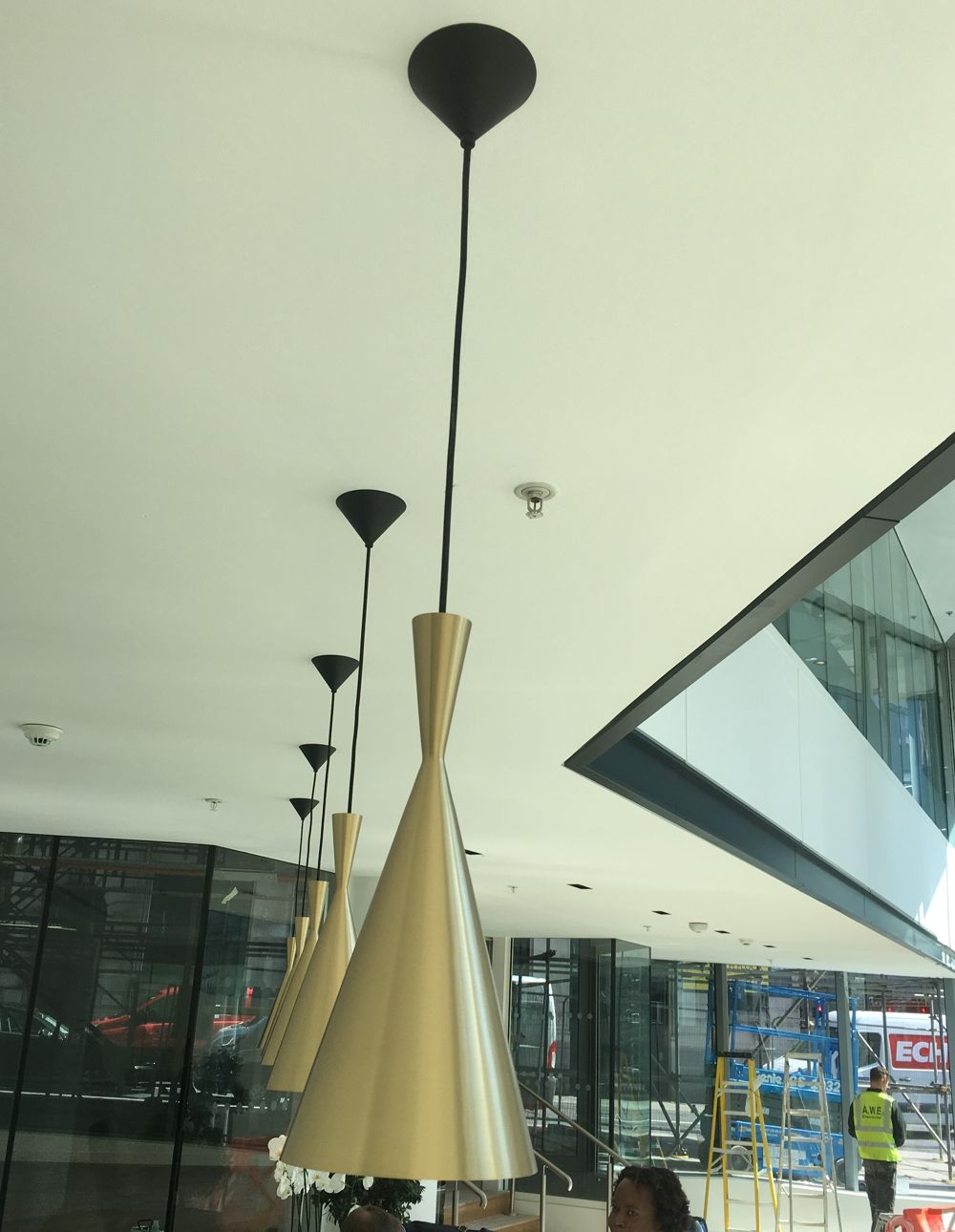 Gold cone pendant lights hang from a white ceiling; modern building exterior visible.