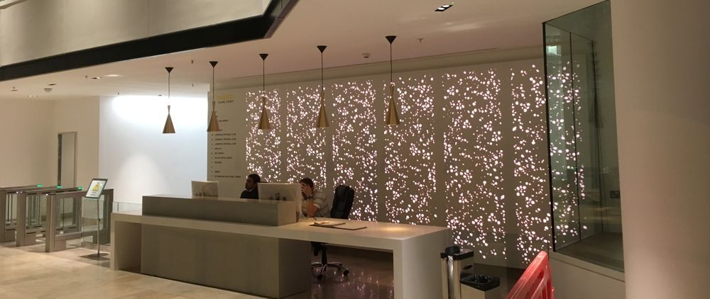 Reception desk with light-colored counter and back wall. Decorative pattern on wall, pendant lights, and security turnstile.